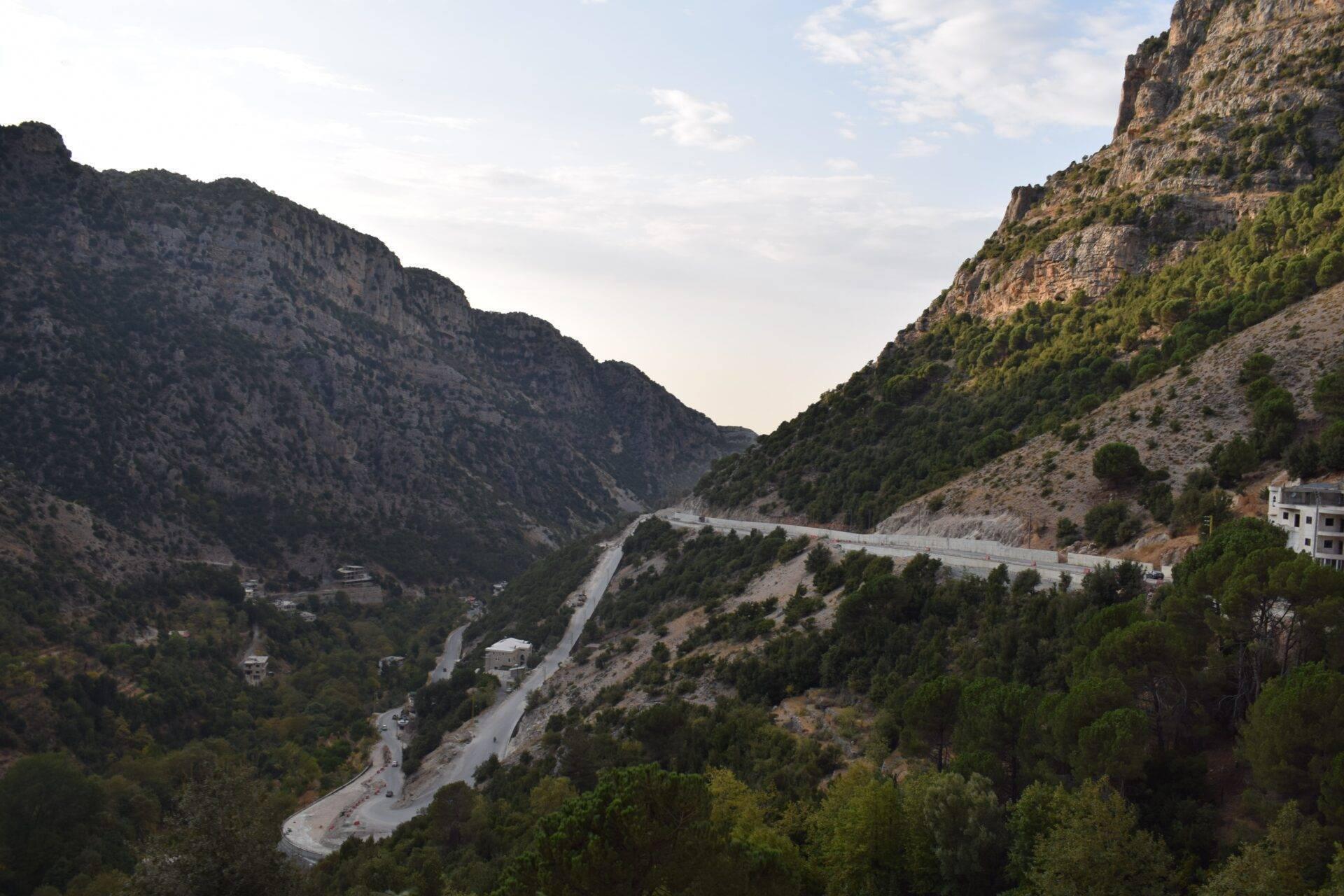Una carretera sinuosa atraviesa un valle montañoso con acantilados rocosos, vegetación mediterránea y viviendas dispersas