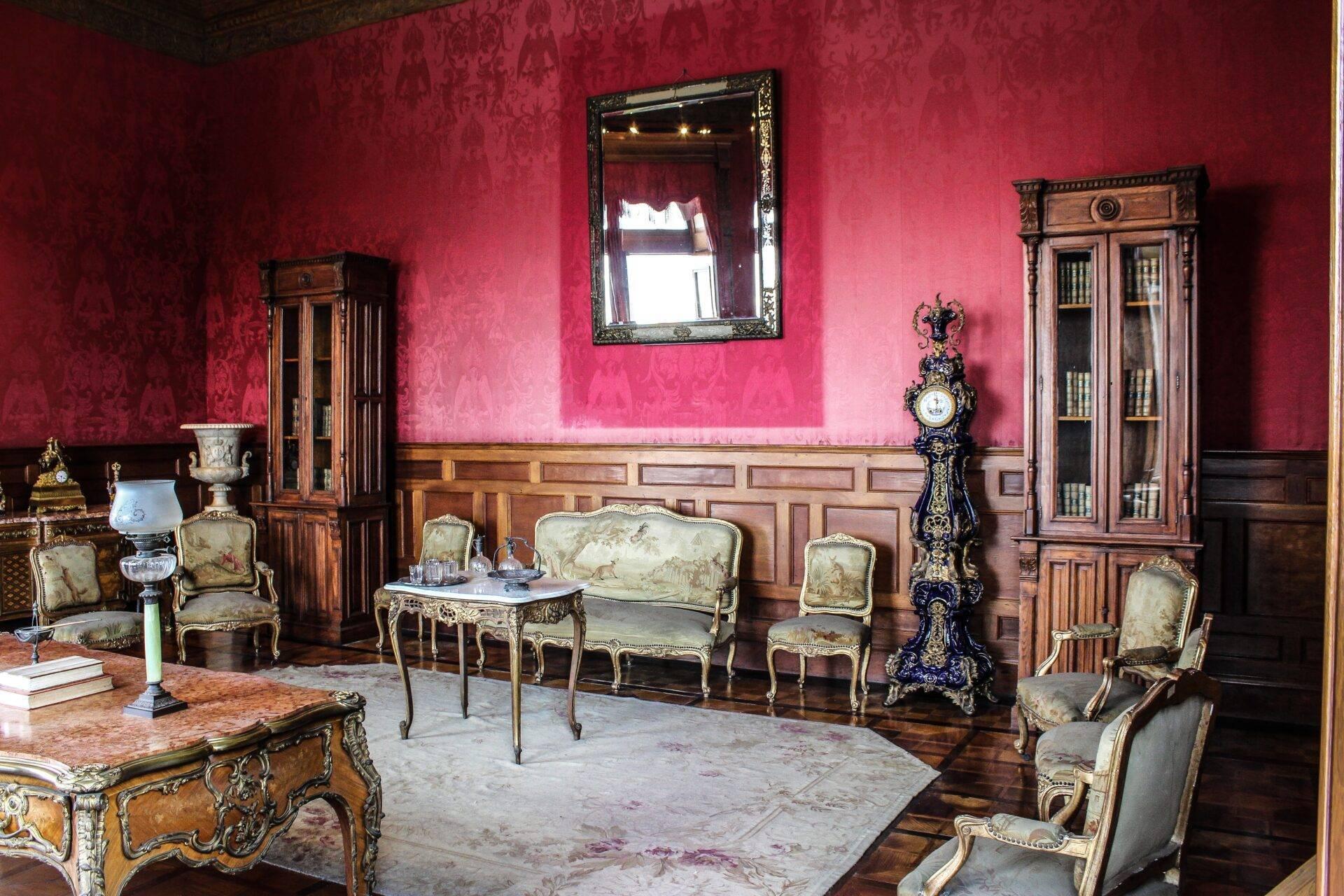Aristokratischer Salon mit leuchtendem Pink an den Wänden, vergoldetem Mobiliar und Holzvertäfelung, Spiegel und verzierte Uhr