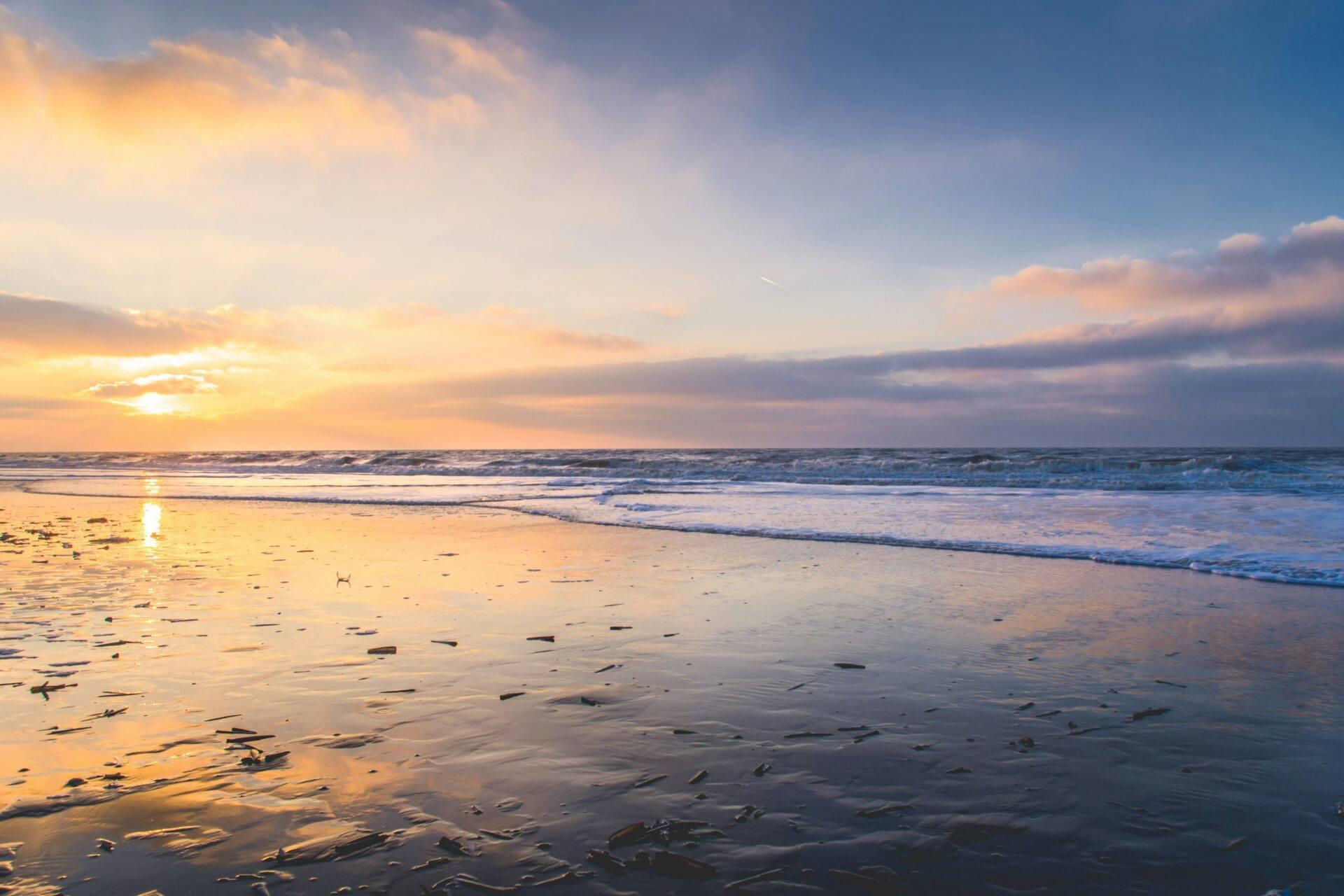 Sonnenuntergang über einem Sandstrand mit Wellen und goldenem orangefarbenen Himmel