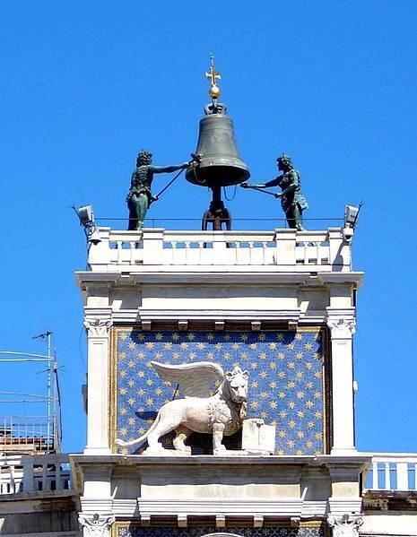 Torre dell’Orologio veneziana con il suo quadrante stellato, la campana e le sculture di bronzo su sfondo di cielo azzurro