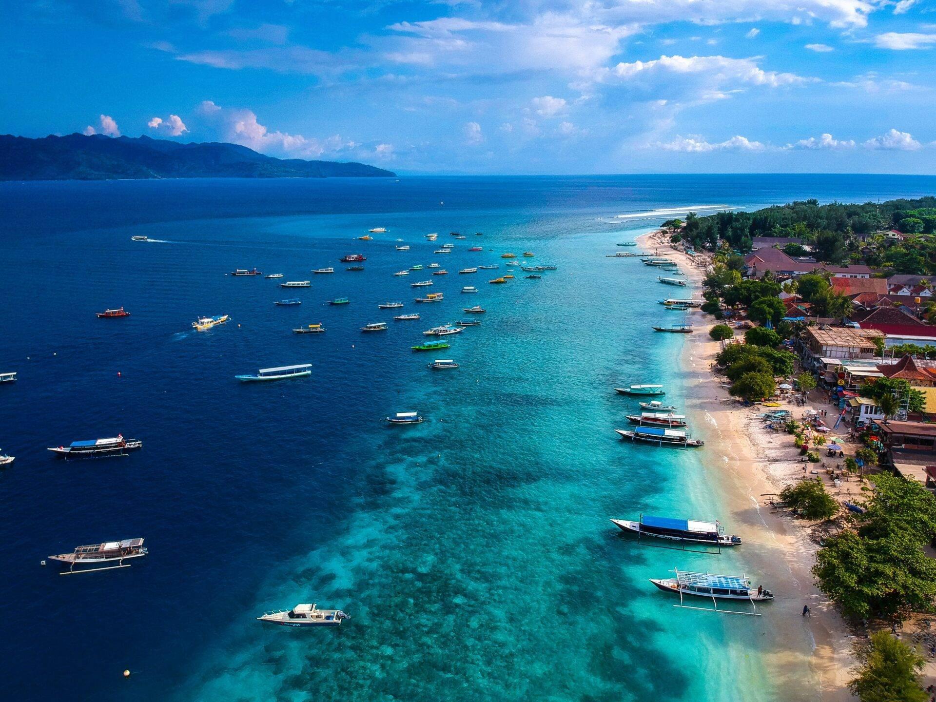 Vista aerea di una baia tropicale con barche a vela colorate ancorate vicino a una spiaggia di sabbia bianca bordata di case