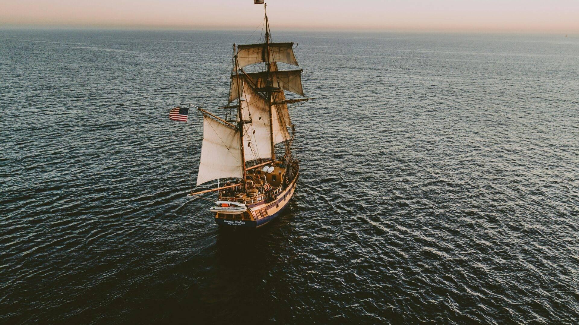 Una nave a vela tradizionale naviga su un mare calmo al tramonto