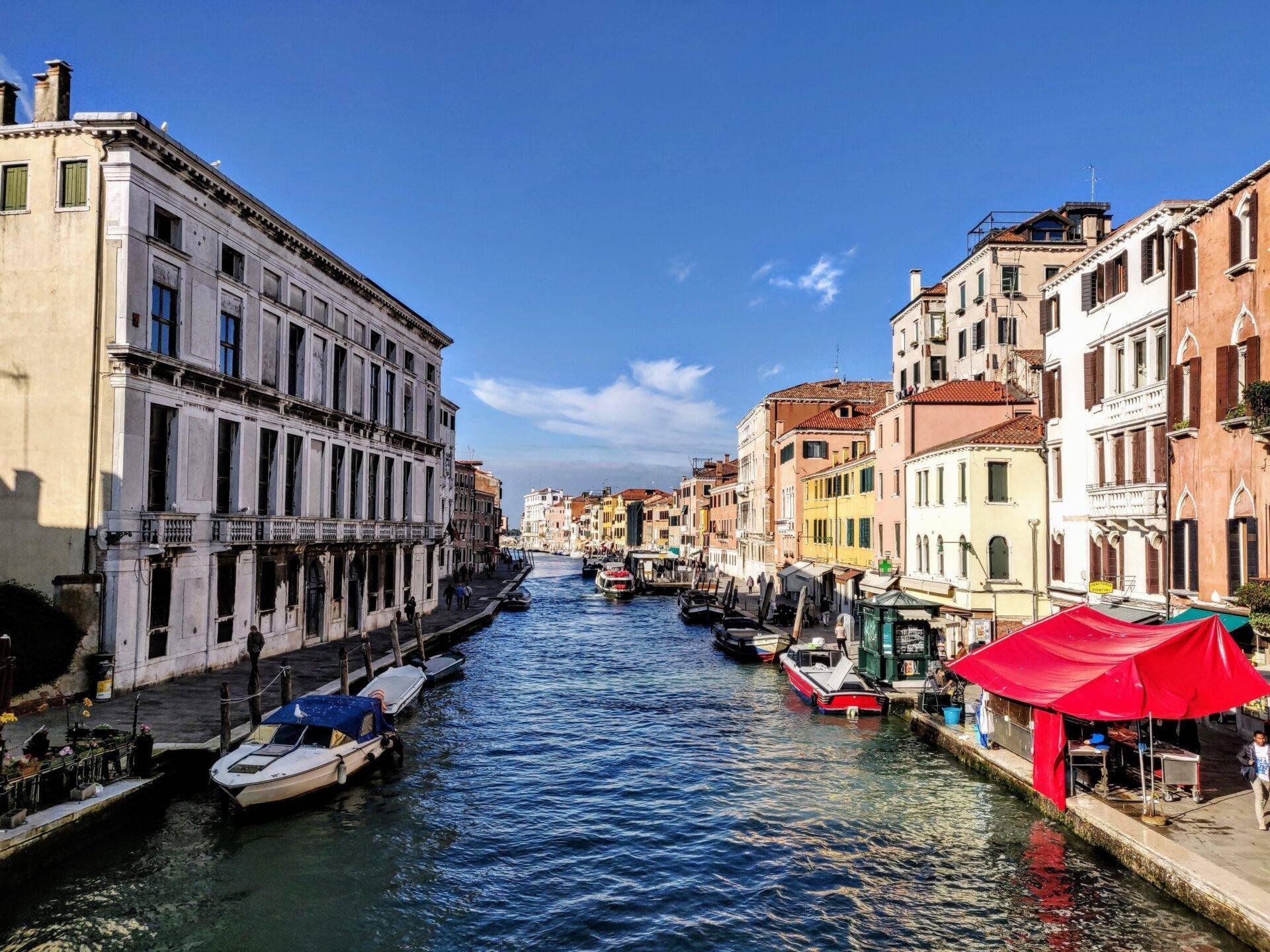 Un canale veneziano fiancheggiato da palazzi colorati con gondole e barche ormeggiate in una bella giornata