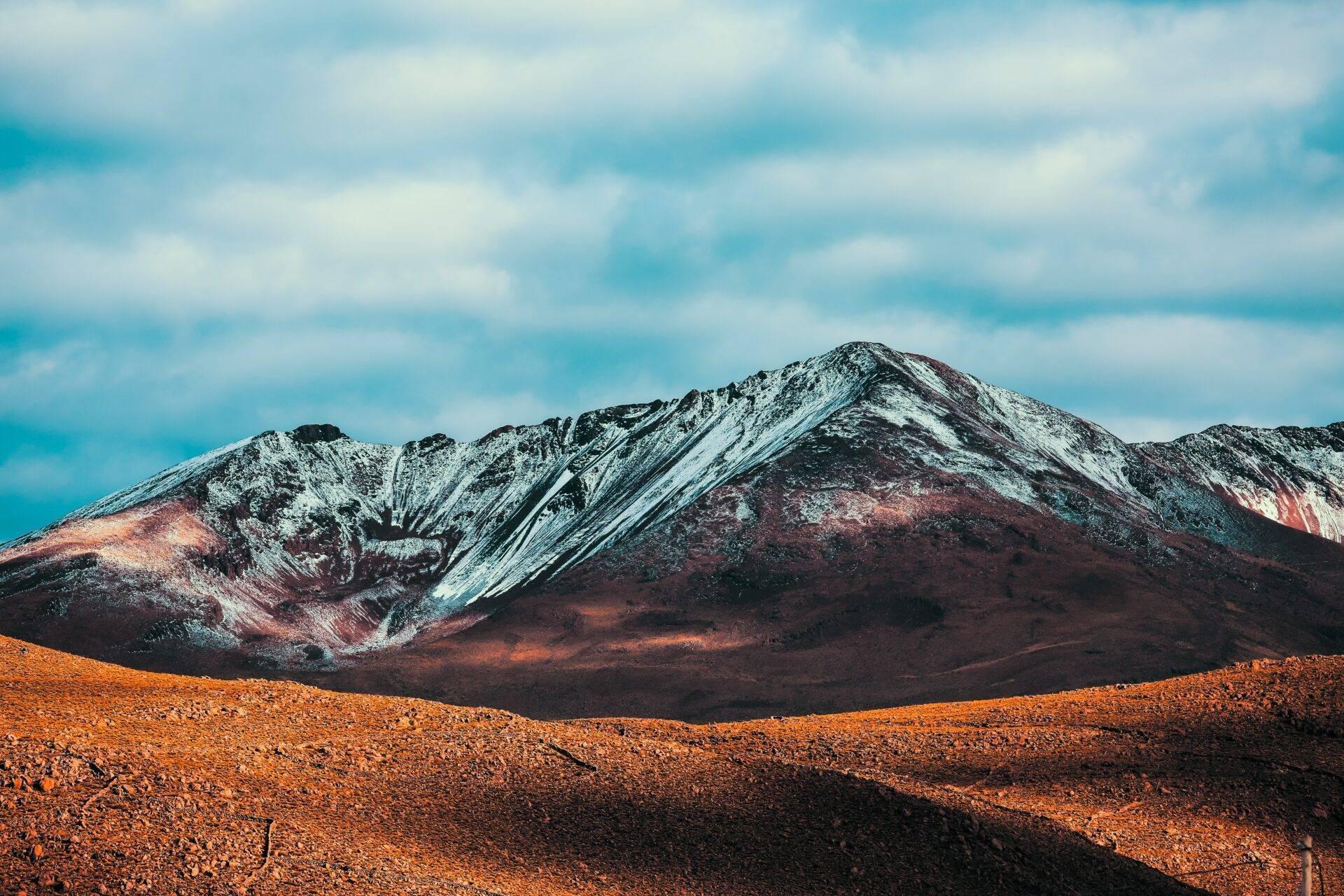 Un vulcano dai fianchi multicolori coperti di neve che domina un deserto roccioso arido sotto un cielo terso
