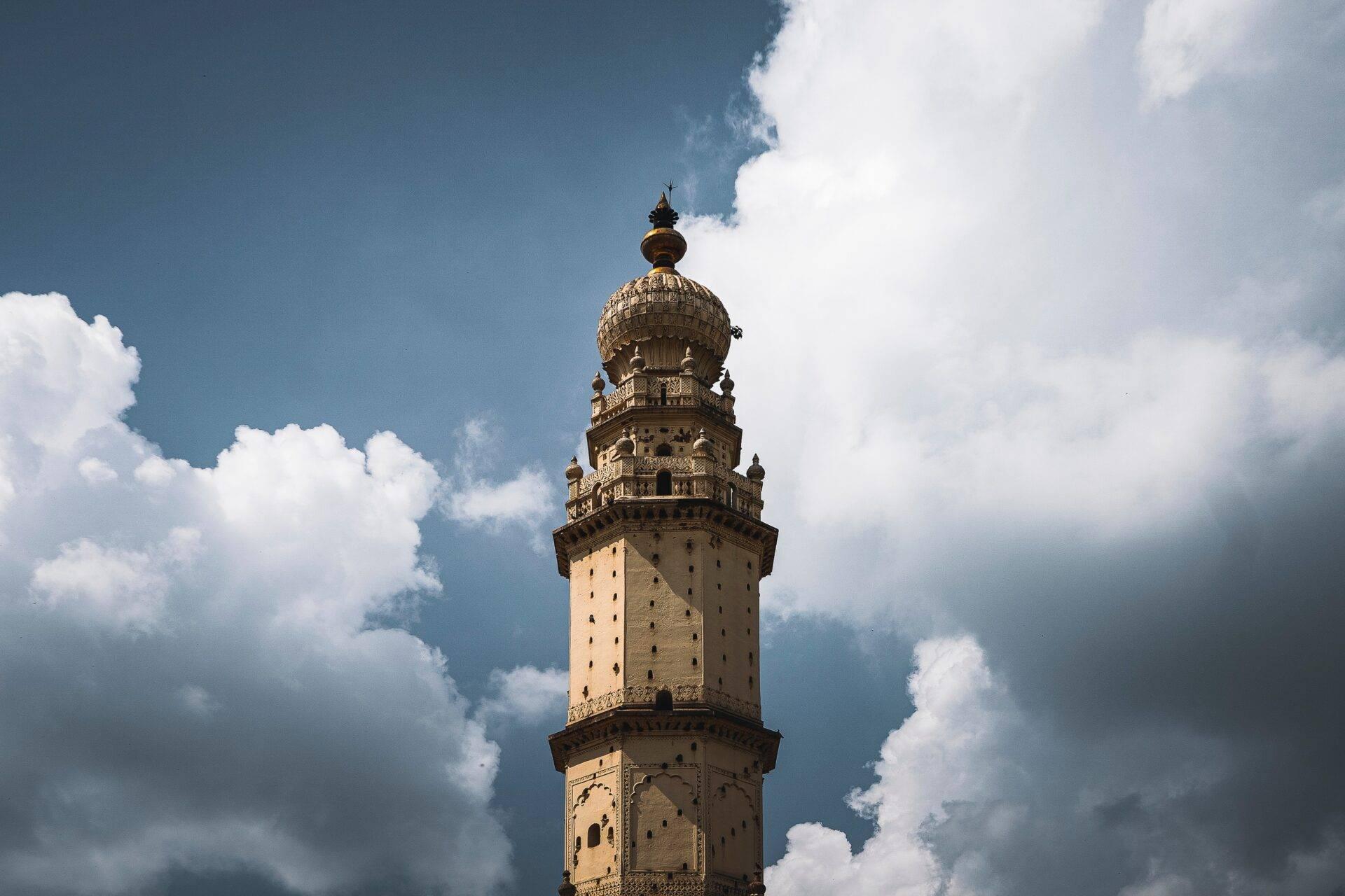 Antico minareto in pietra ocra con balconi ornamentali sotto un cielo azzurro nuvoloso