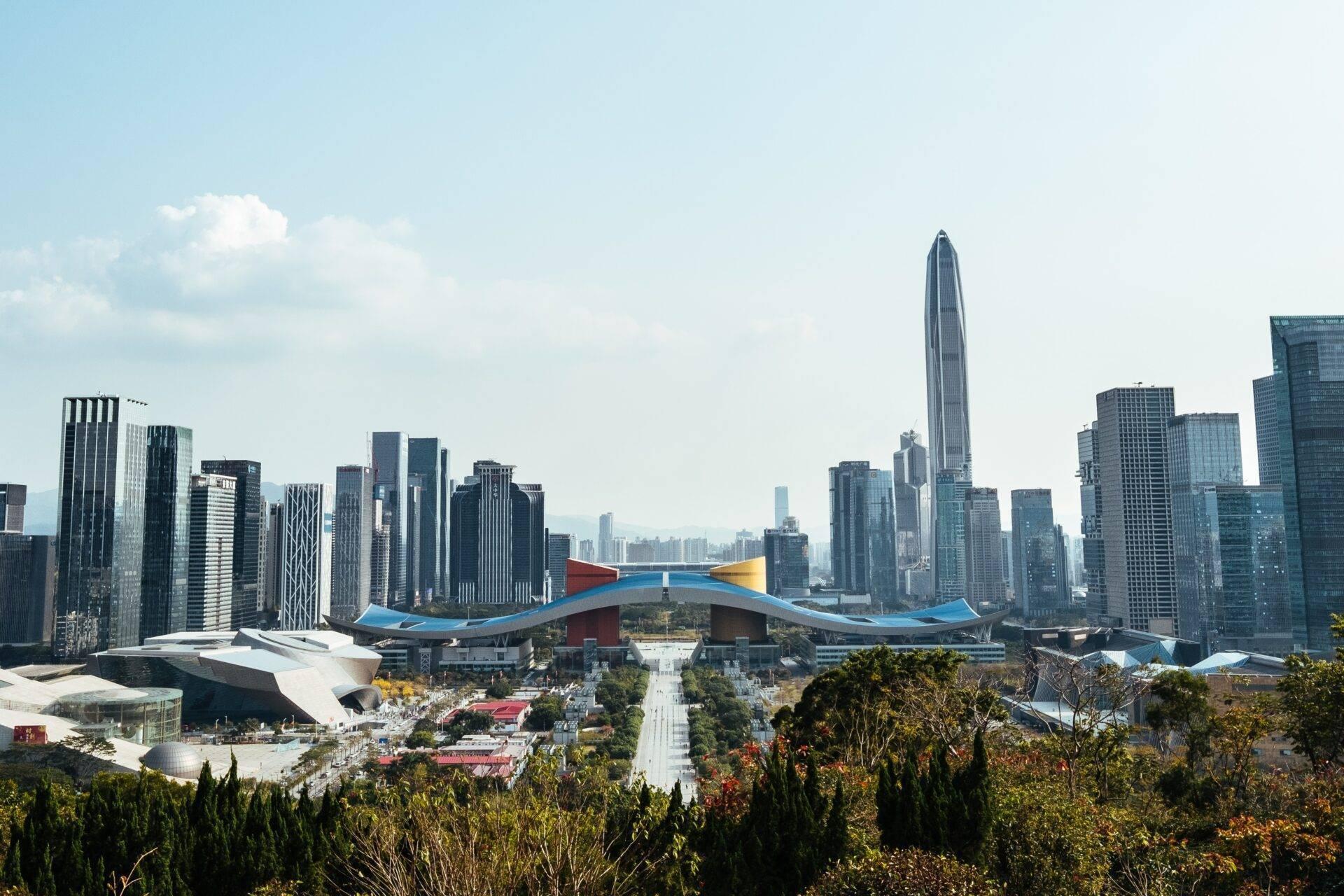 Vista panoramica di una città moderna con grattacieli, edificio architettonico blu e rosso in primo piano, parco verdeggiante e cielo terso