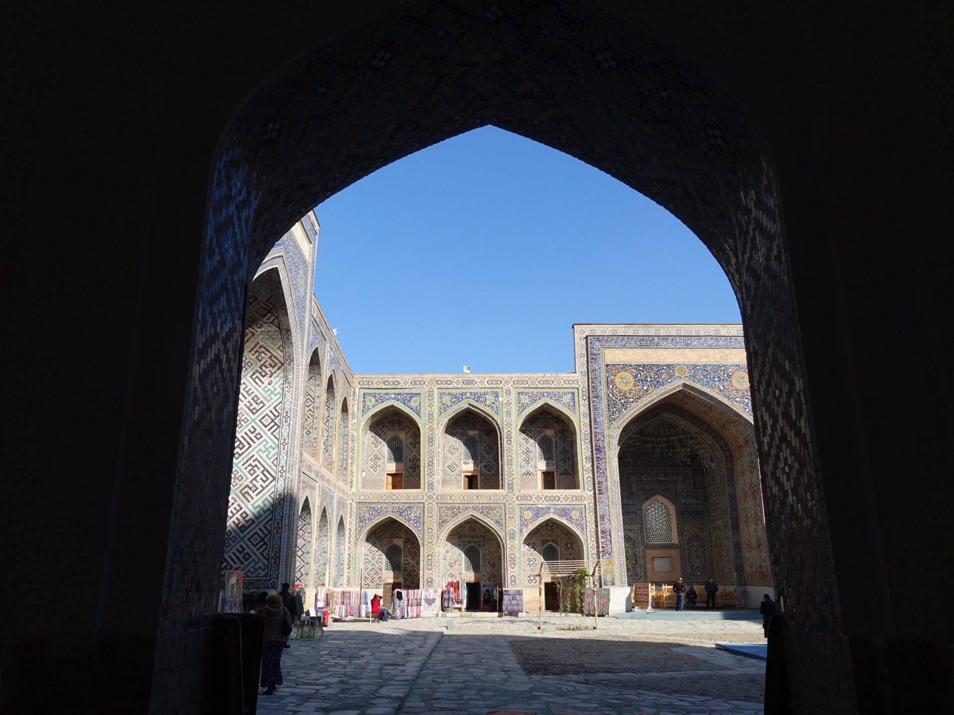 Blick durch einen Eingangsbogen auf einen mit blauen Mosaiken und islamischen geometrischen Mustern verzierten Innenhof