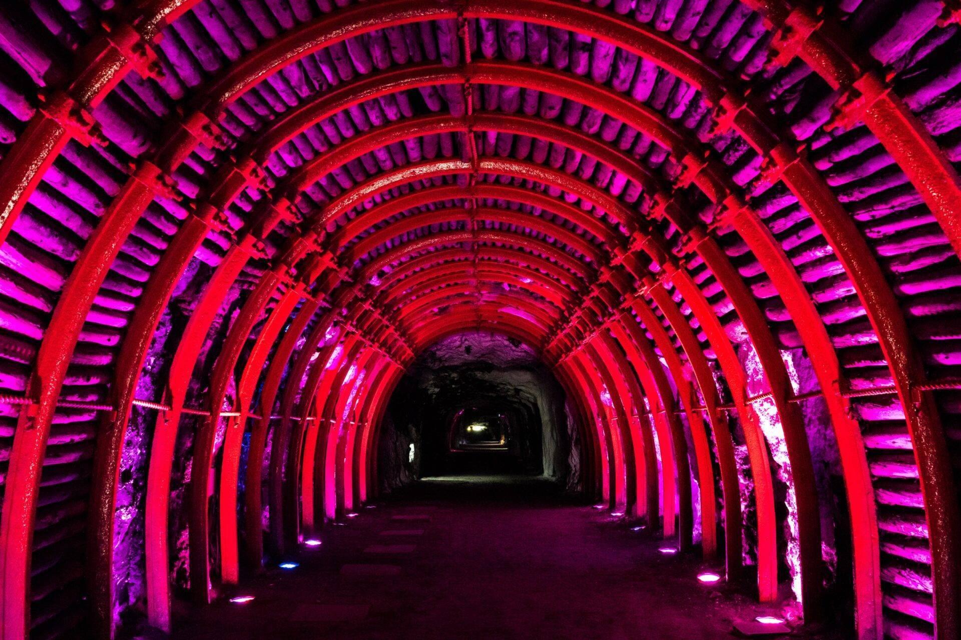 Túnel subterráneo iluminado por neones rosas y rojos con sucesivos arcos metálicos