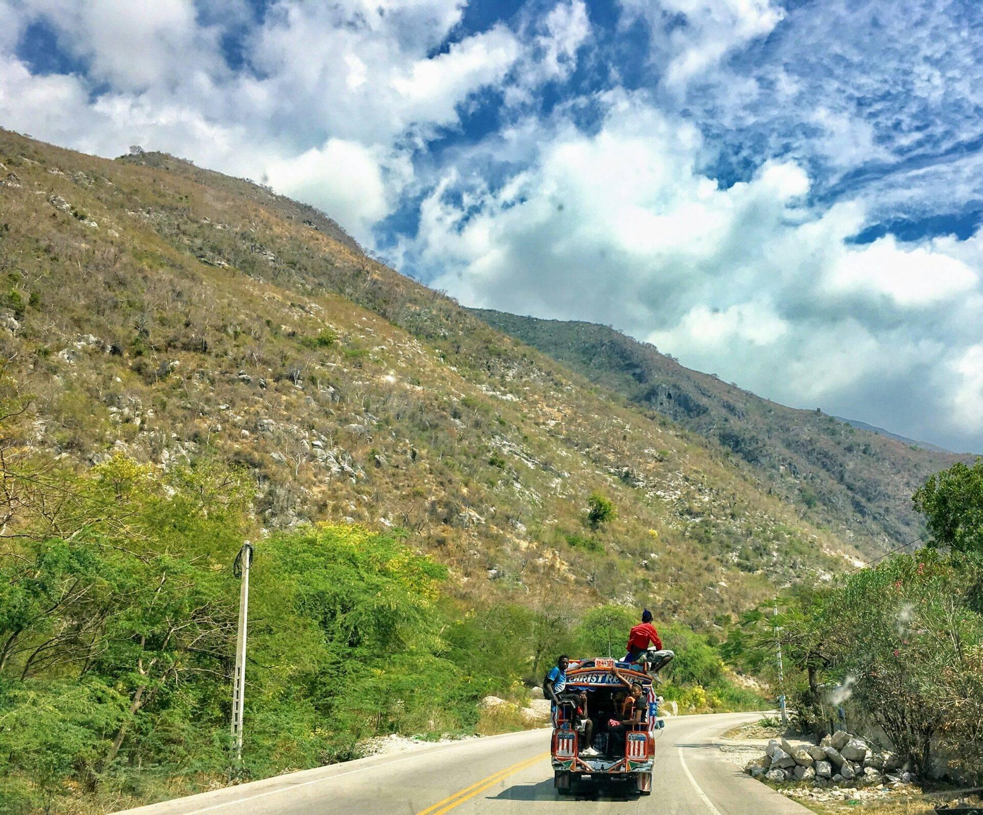 Un camión de colores circulando por una carretera de montaña rodeada de exuberante vegetación y colinas boscosas