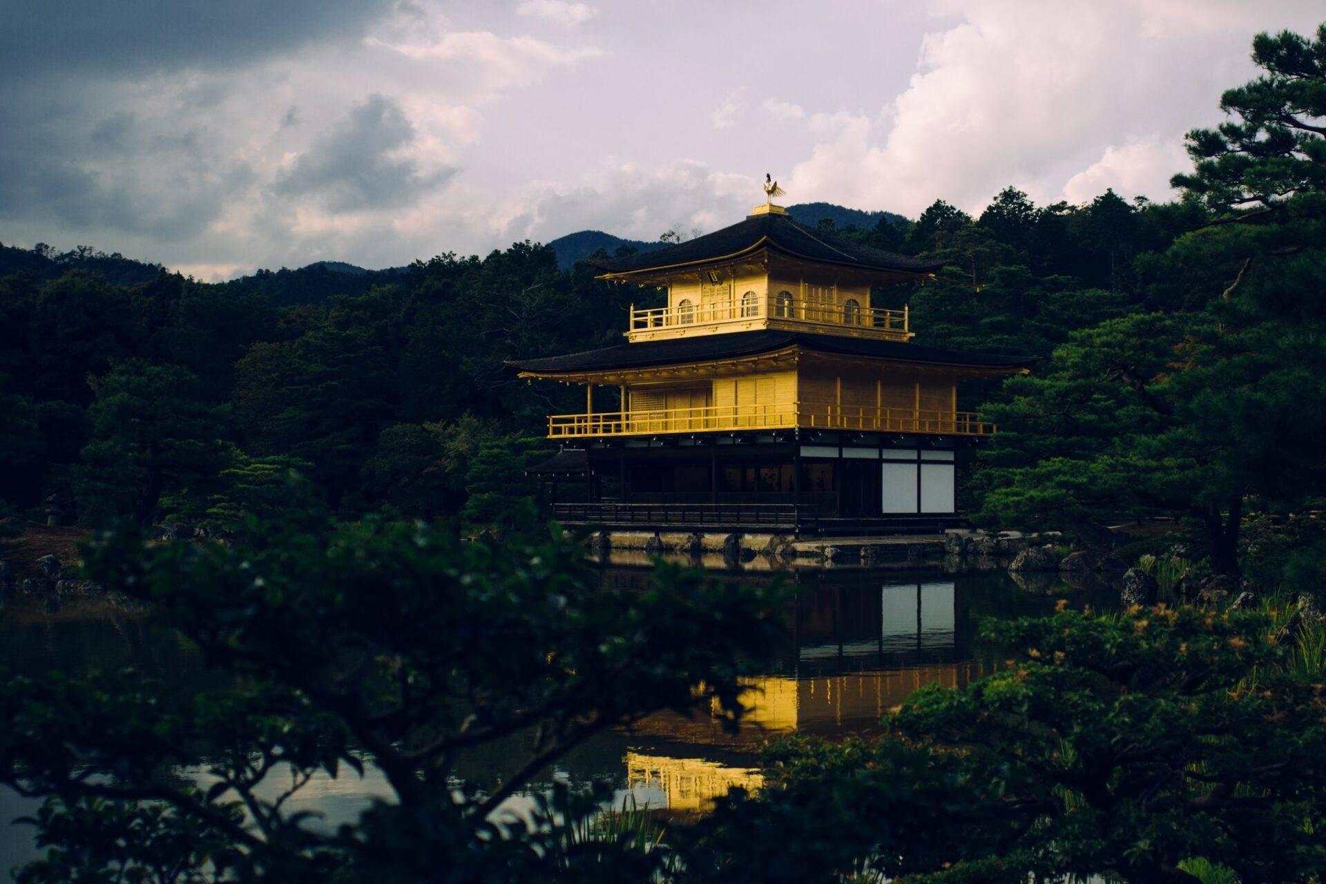 Ein zweistöckiger goldener Pavillon spiegelt sich in einem ruhigen Teich, umgeben von Grün und bewaldeten Bergen