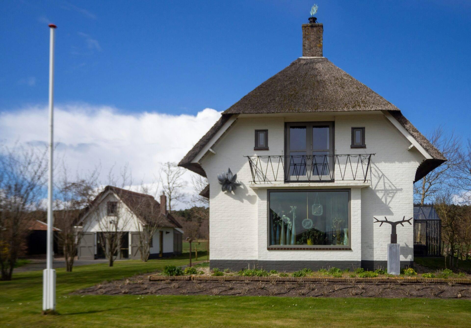 Traditionelles weißes niederländisches Haus mit spitzem Reetdach und schmiedeeisernem Balkon