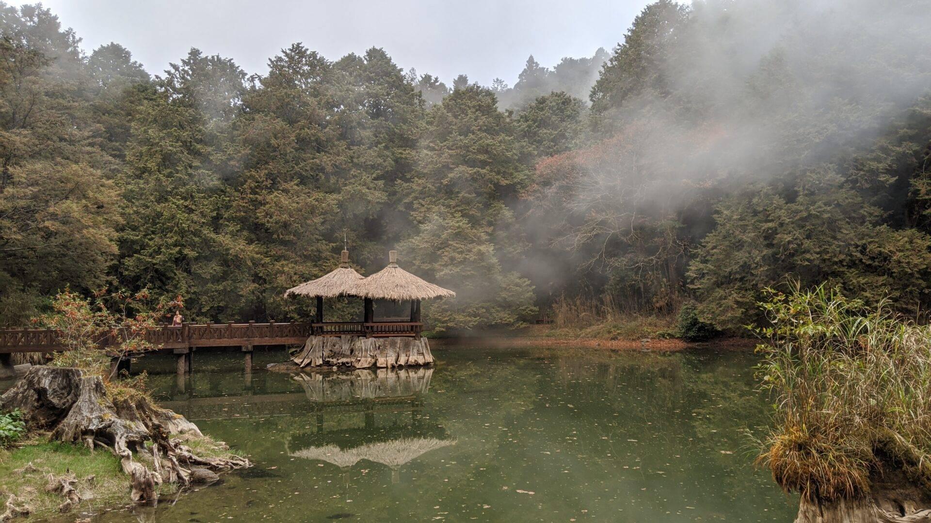 Padiglione tradizionale con tetti di paglia su un lago circondato da foreste montuose nella nebbia mattutina