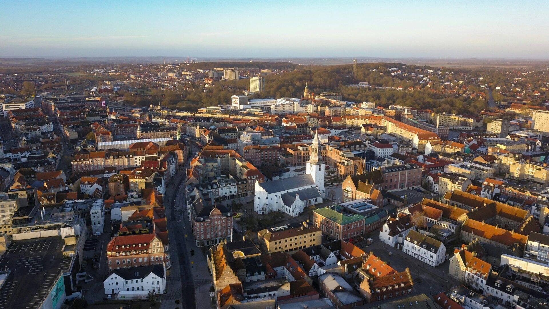 Vista aerea di una città europea con chiese, tetti arancioni e spazi verdi sullo sfondo