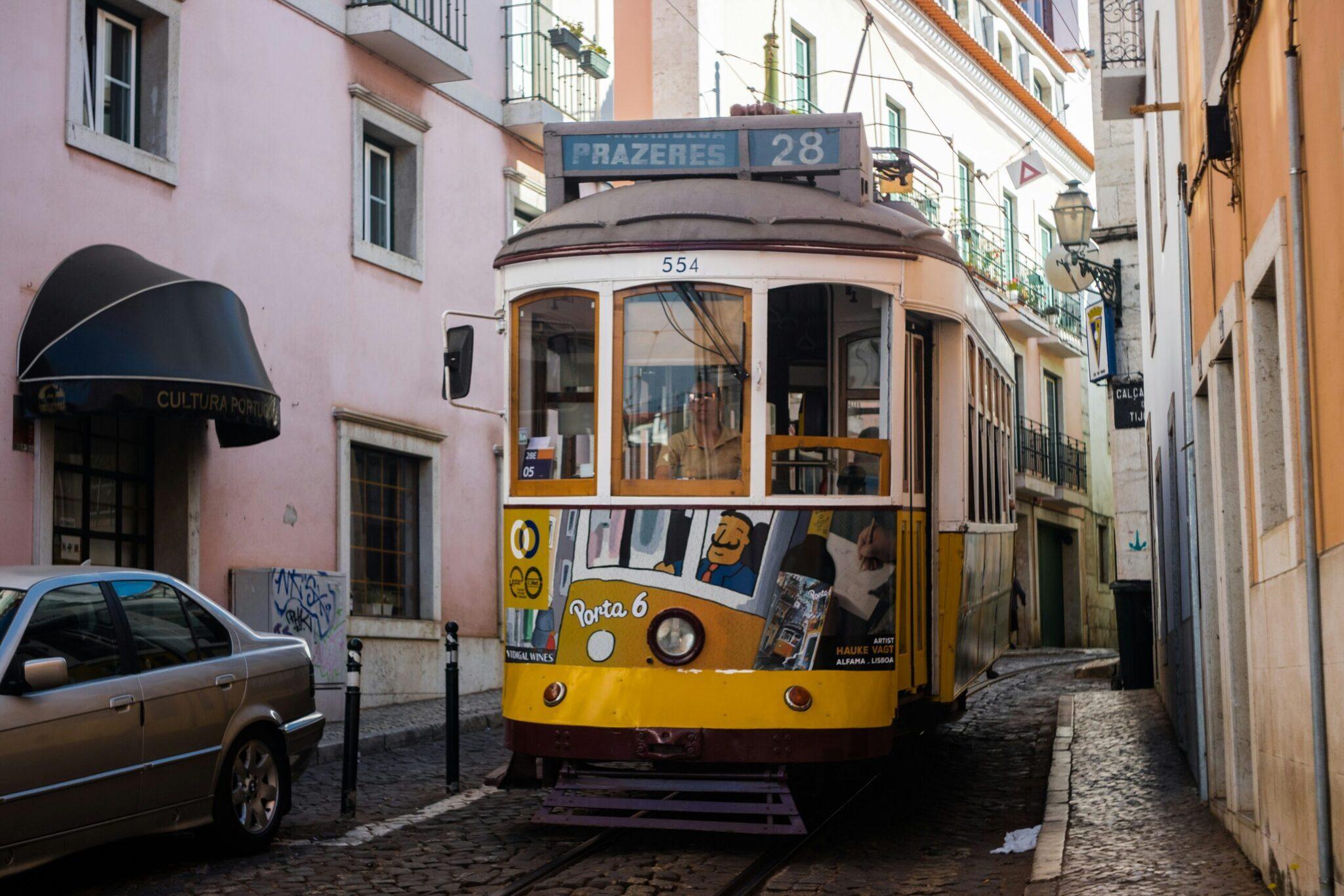 Die berühmte gelbe Straßenbahn Nummer 28 in einer engen gepflasterten Gasse des historischen Lissaboner Stadtviertels