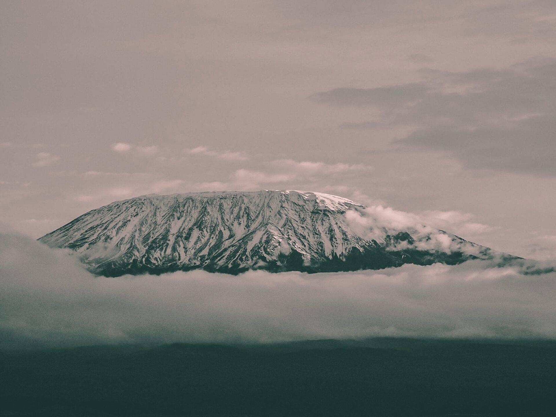 Ein schneebedeckter Gipfel mit gefurchten Hängen ragt teilweise aus den Wolken, majestätische Hochgebirgslandschaft in großer Höhe