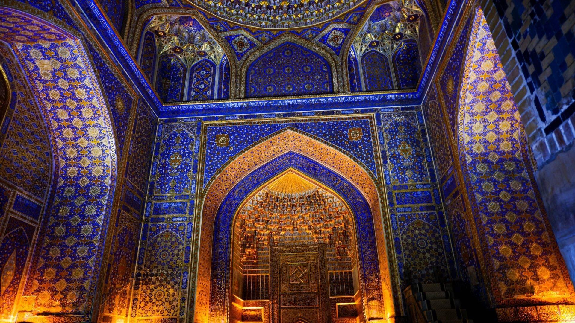 Prächtig verzierter Innenraum einer Moschee mit kobaltblauen Wänden, goldenen Ornamenten und einem monumentalen beleuchteten Portal
