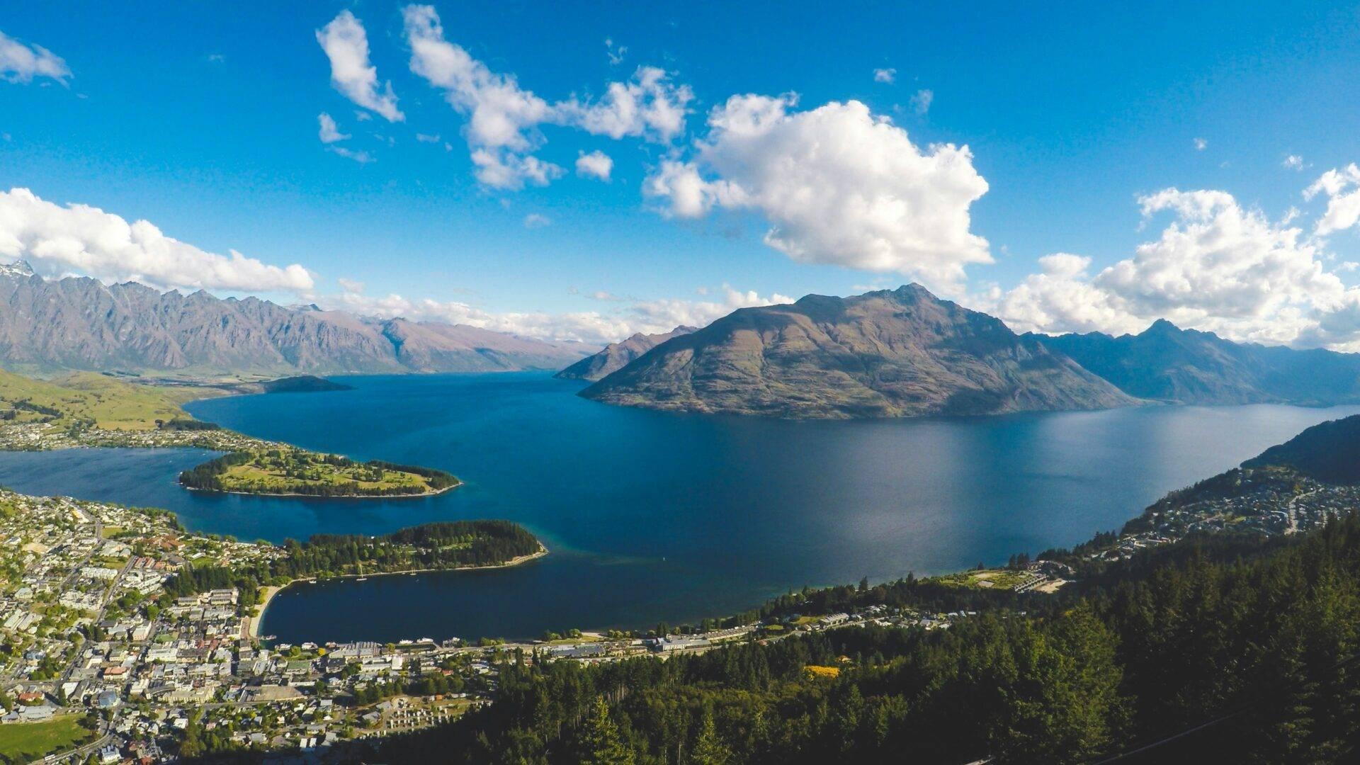 Vista aerea di un lago alpino turchese circondato da montagne, foreste e paesi costieri sotto un cielo blu