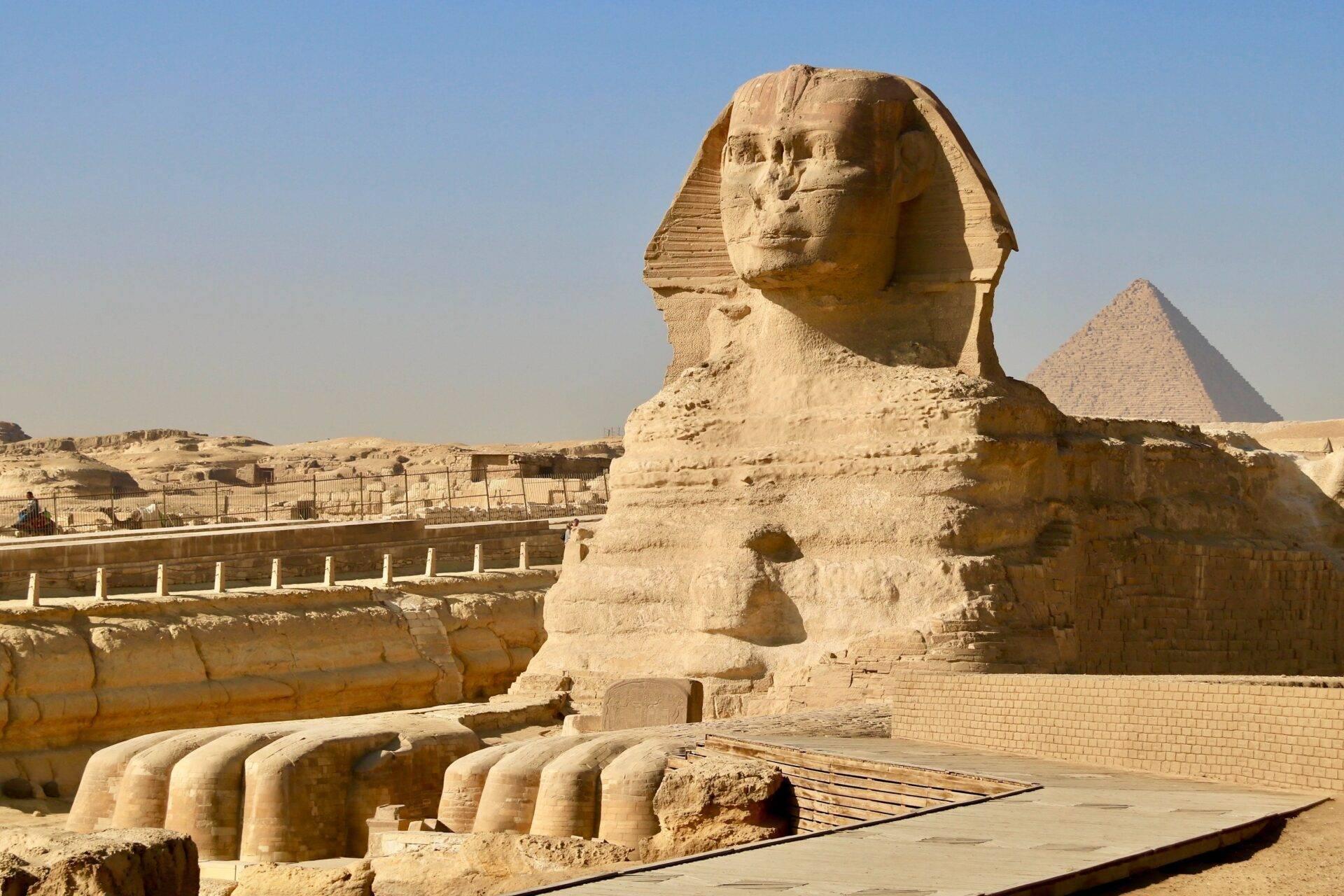 La Grande Sfinge di Giza di fronte a una piramide, con resti architettonici e barriere di protezione