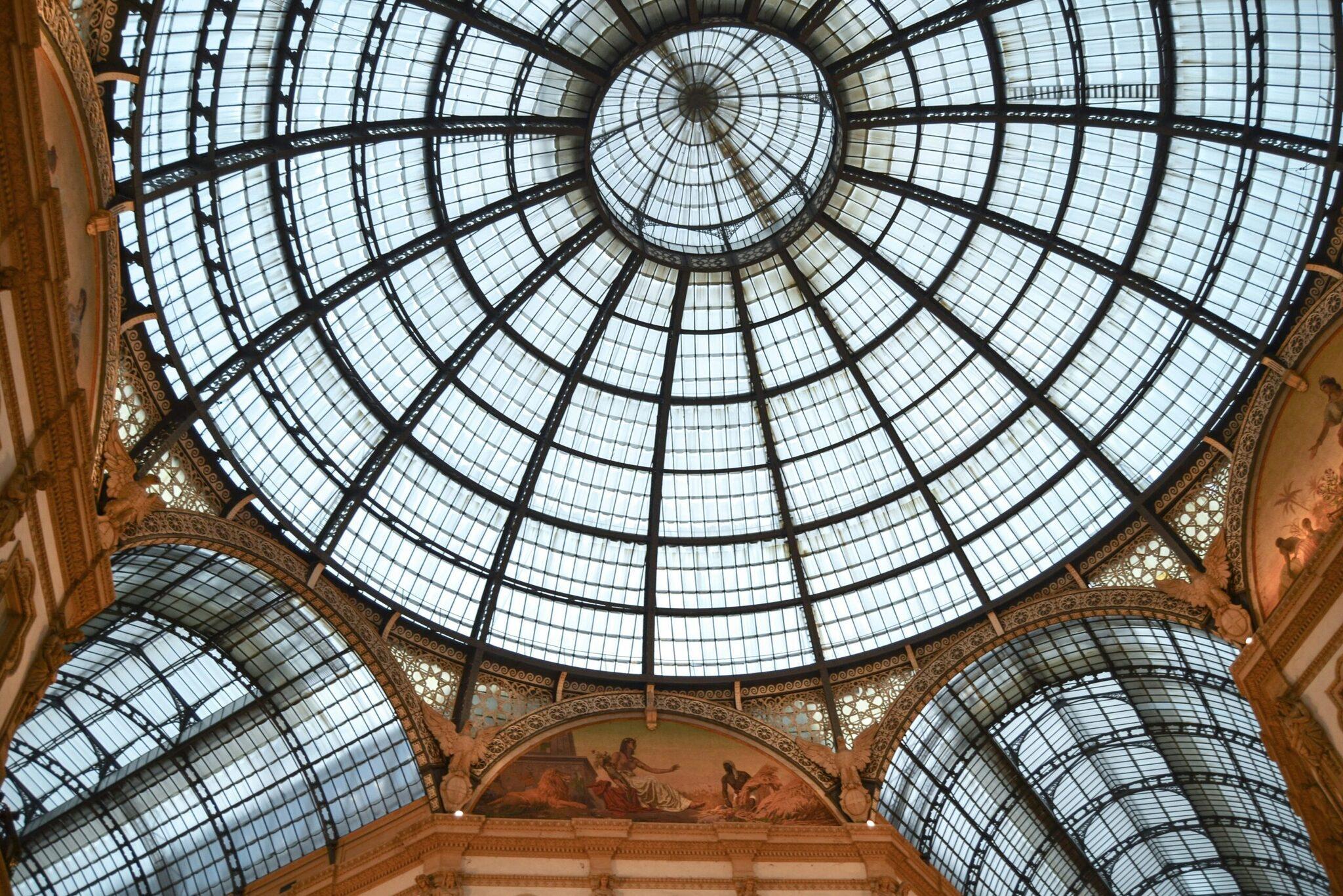 Geometrisches Glasdach einer historischen Einkaufspassage mit goldenen Verzierungen und Wandfresken