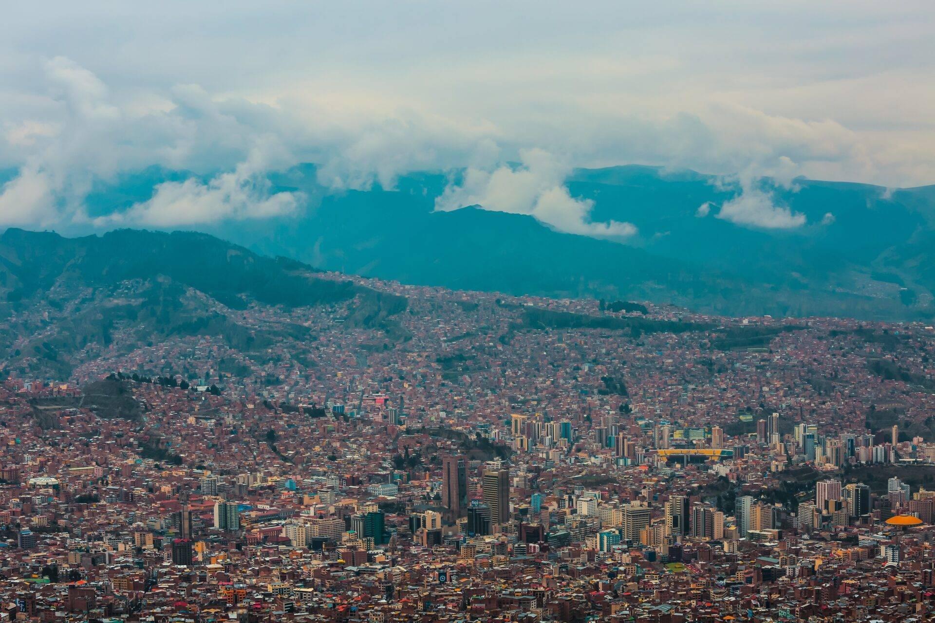 Veduta aerea di una grande città andina densamente costruita, incorniciata da montagne verdeggianti sotto un cielo nuvoloso