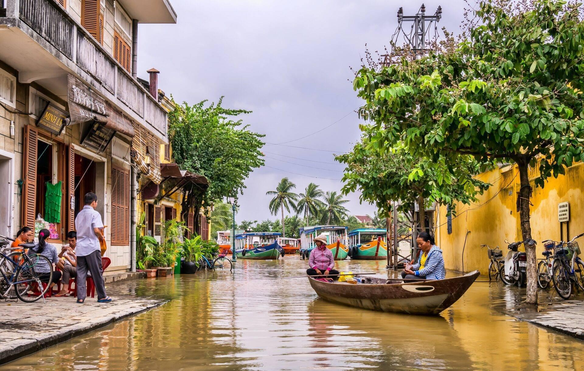 Una calle inundada de una ciudad vietnamita con barcas, casas de colores y habitantes circulando en bicicleta