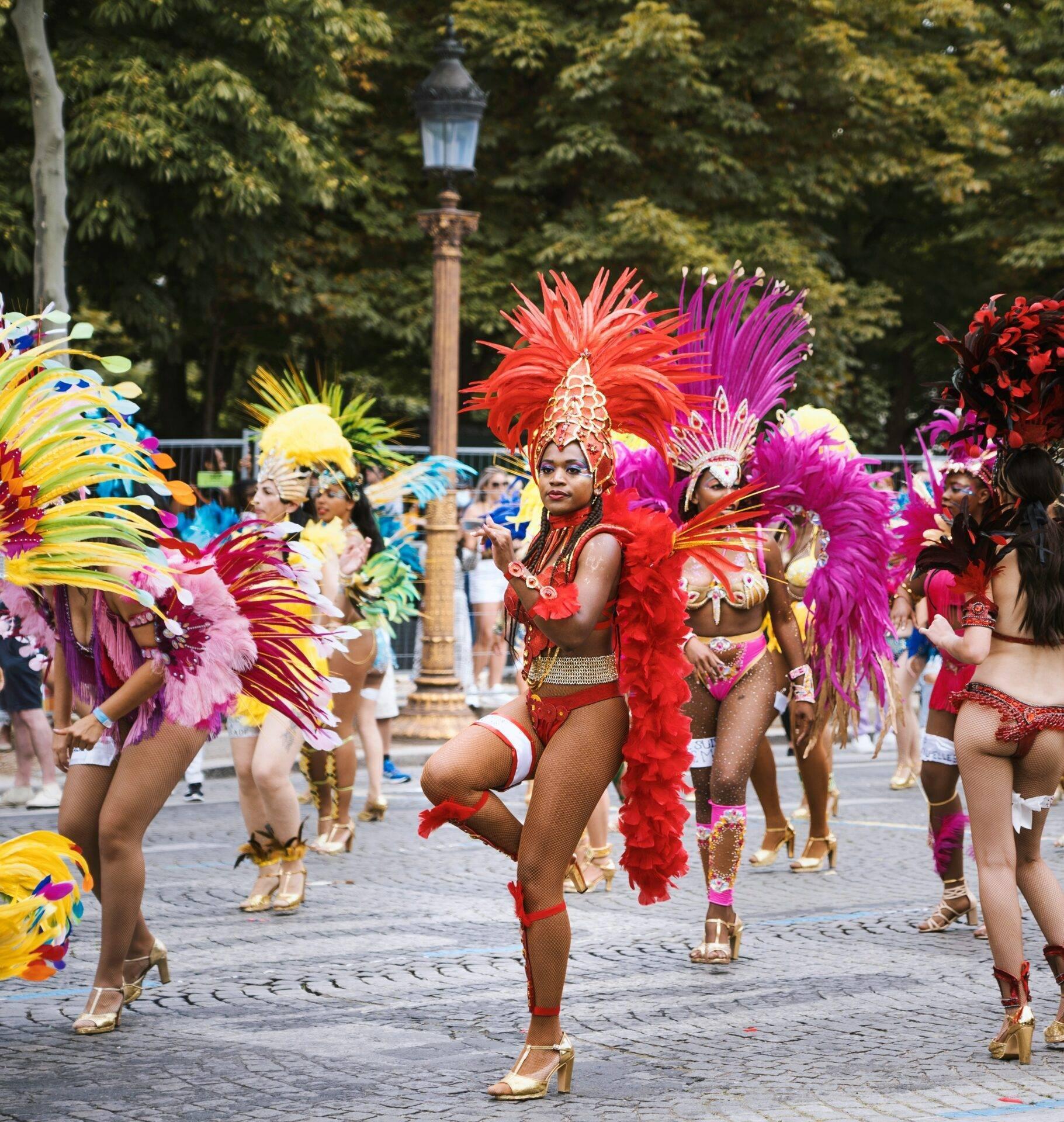 Sfilata di carnevale con ballerine in costumi colorati e piumati, strada lastricata, lampione sullo sfondo