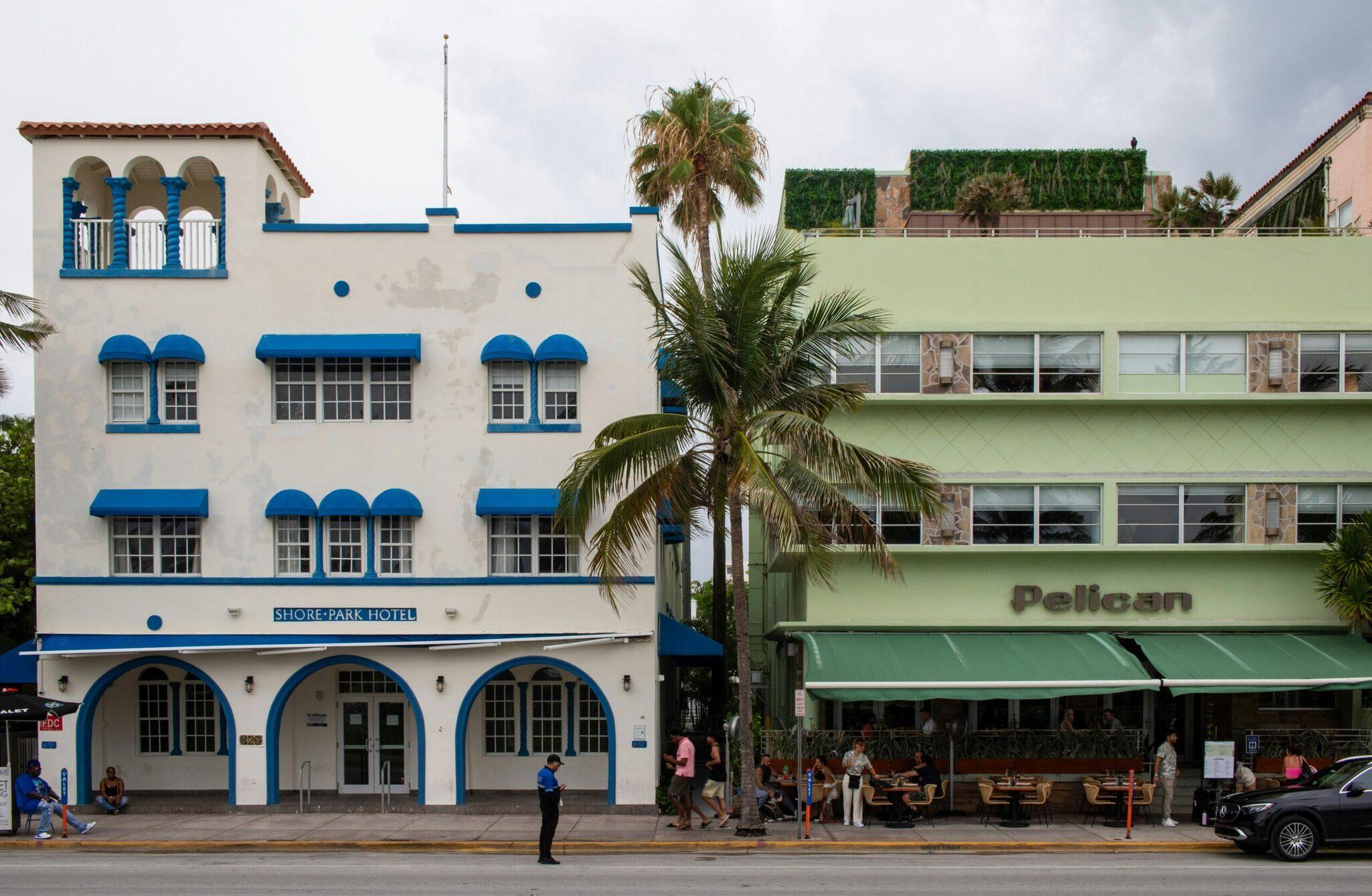 Colourful white and blue Art Deco facades with palm trees lining a busy Miami Beach street