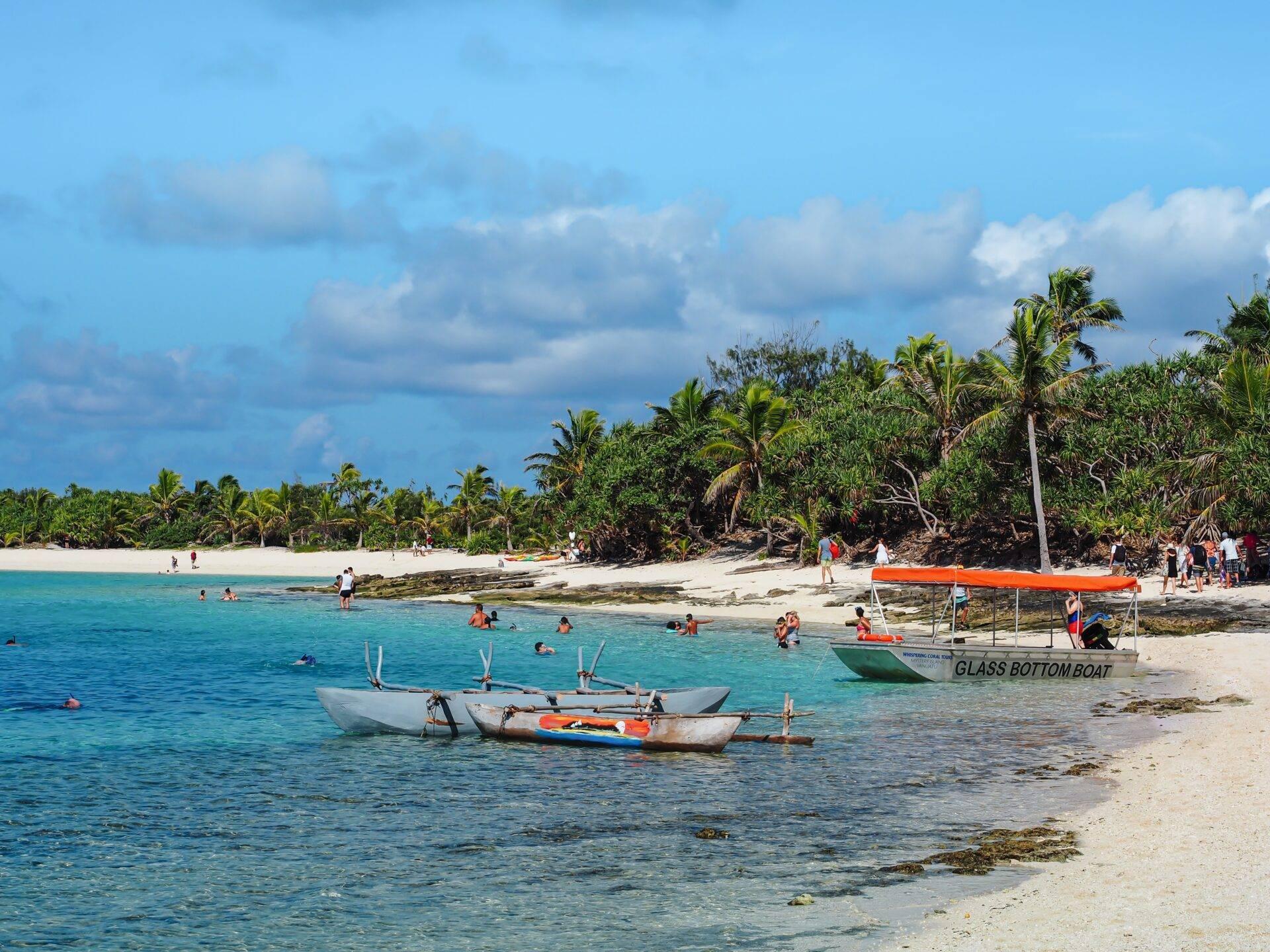 Tropischer Strand mit traditionellen Fischerbooten, Badenden und Palmen unter teils bewölktem Himmel