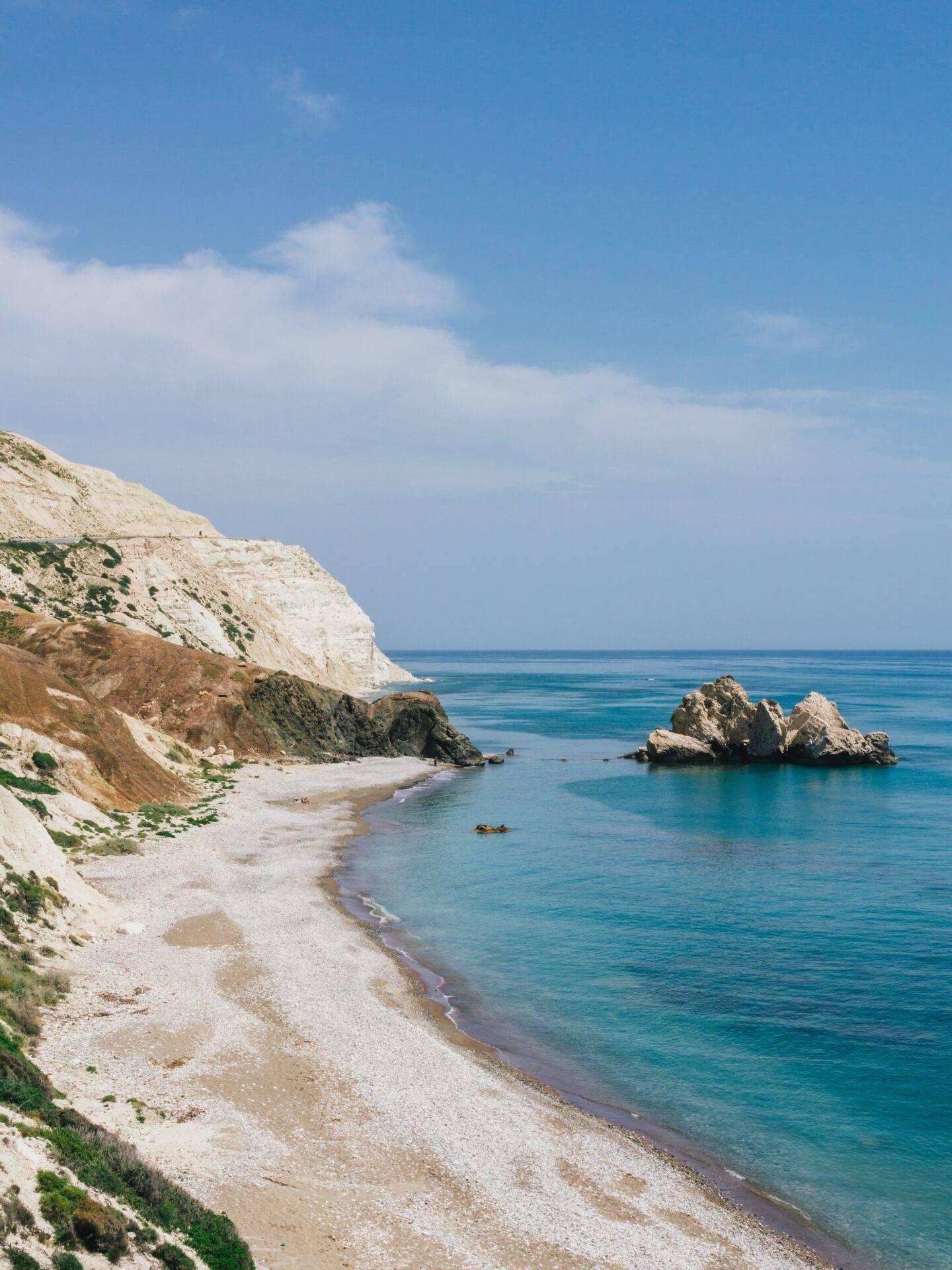 Ein Strand aus reinweißen Kieseln, gesäumt von Kalksteinfelsen, vor einem kristallklaren türkisfarbenen Mittelmeer