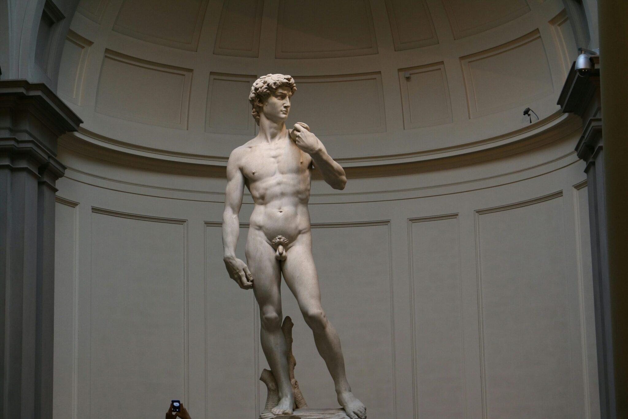 Estatua de mármol blanco de un joven desnudo en una galería de paredes gruesas y techo abovedado