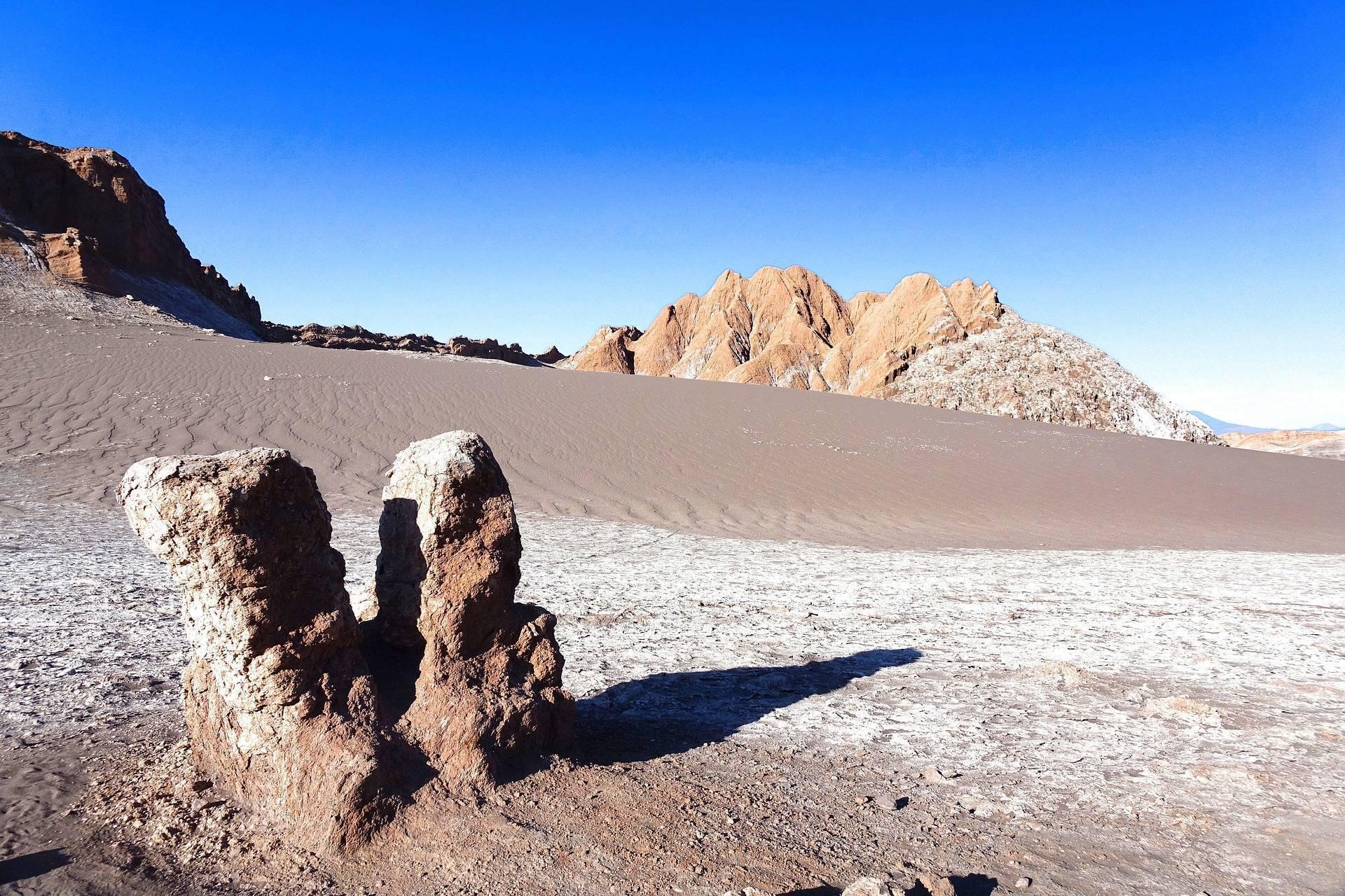 Formación rocosa singular en un desierto árido con montañas de colores bajo un cielo azul despejado