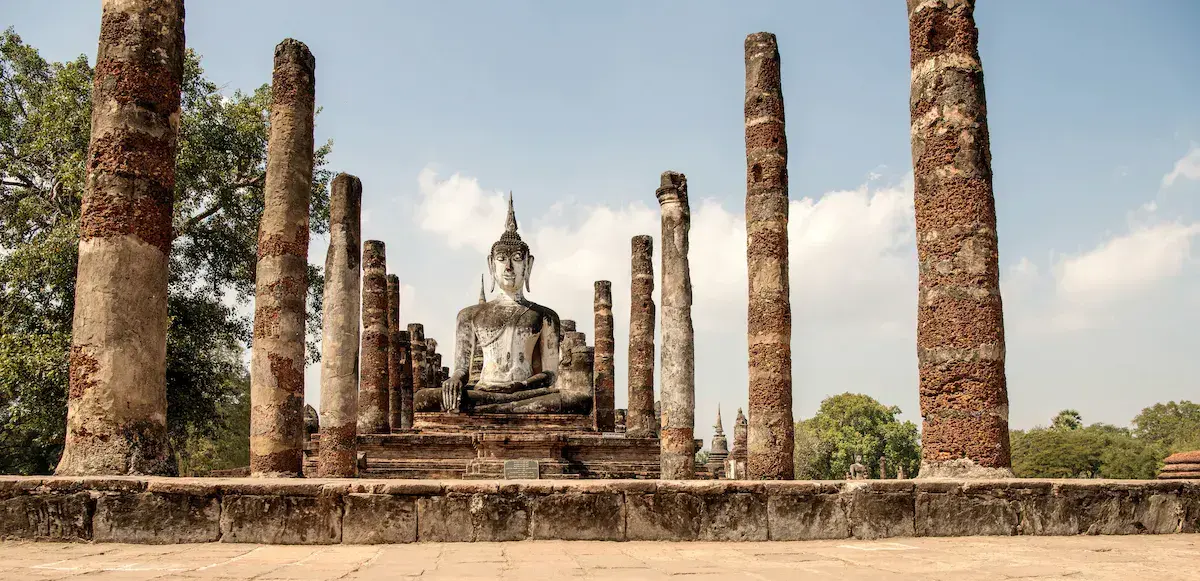 Estatua de Buda sentado rodeada de columnas de piedra en las ruinas de un antiguo templo tailandés