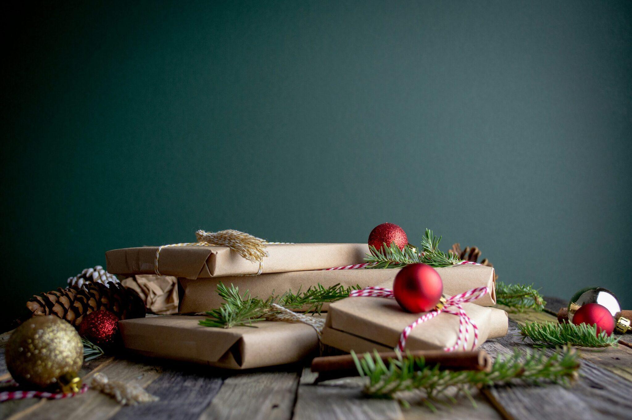 Composición de regalos envueltos en papel kraft con cintas rosas y blancas, decorada con bolas rojas, abeto y piñas sobre madera