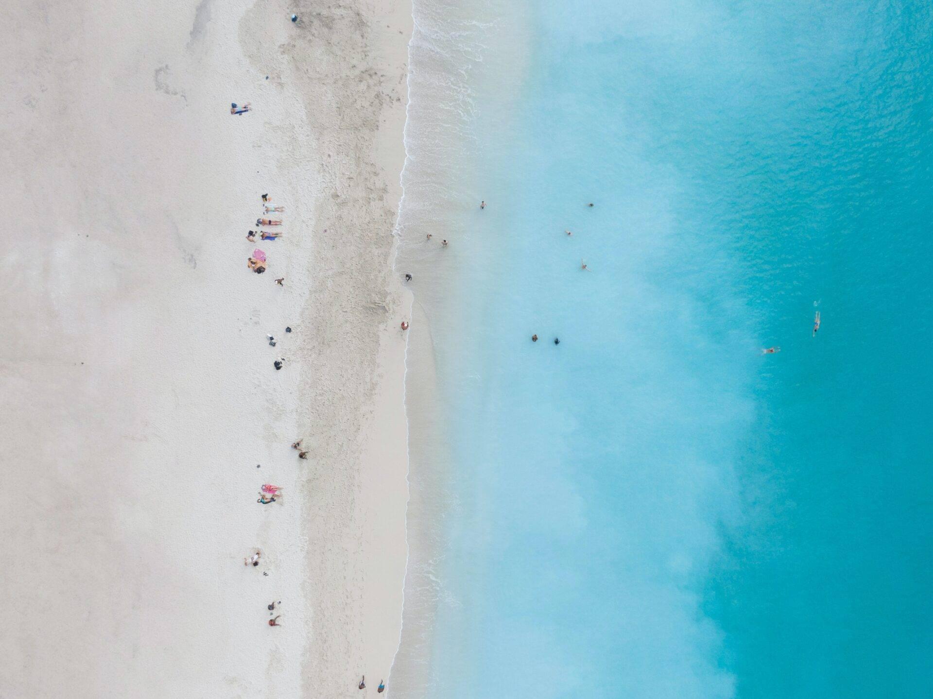 Vue aérienne d’une plage de sable blanc avec baigneurs dispersés et eaux turquoise cristallines