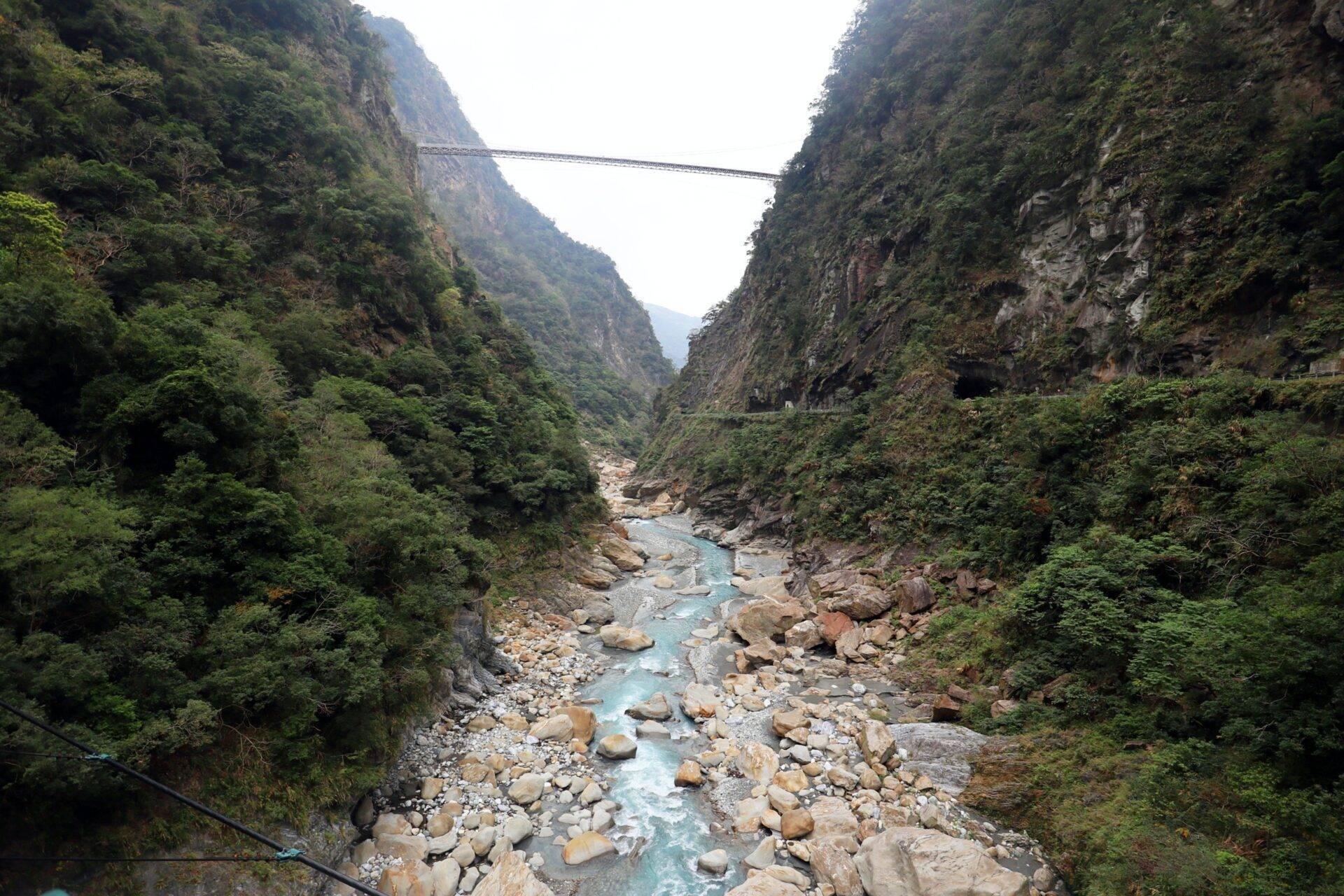 Una gola montuosa profonda attraversata da un fiume turchese, incorniciata da scogliere verdeggianti e un ponte sospeso