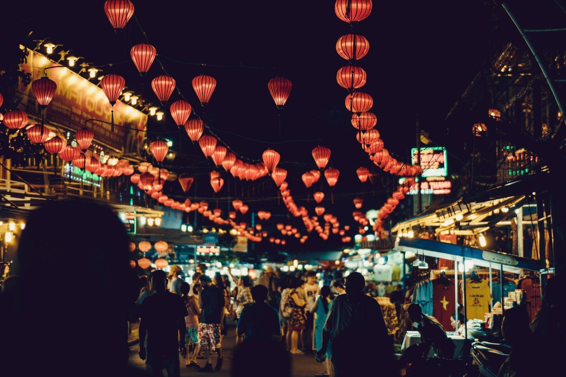 Una calle comercial animada de noche, iluminada por faroles rojos tradicionales y fachadas luminosas