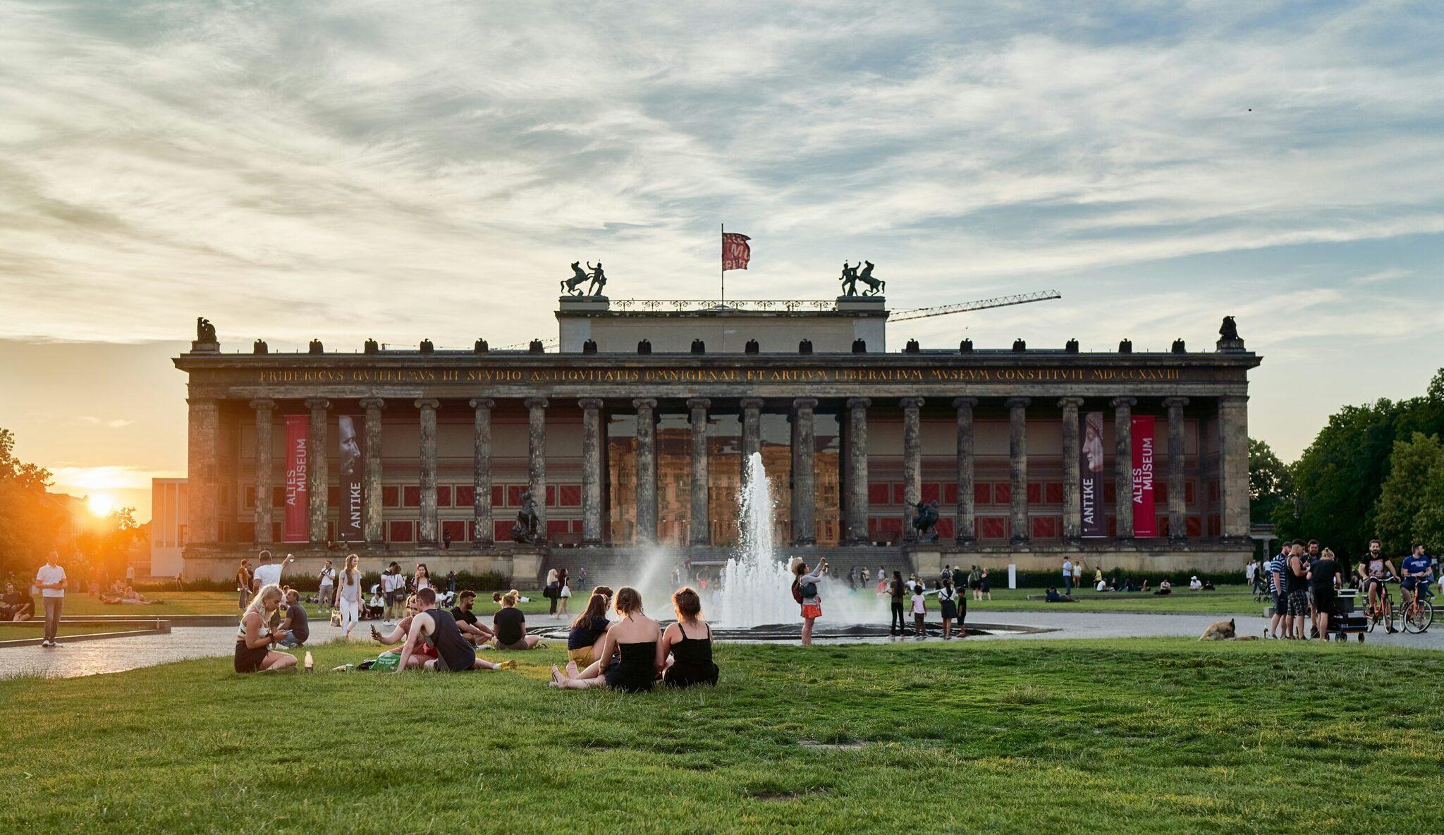 Museo neoclásico con imponentes columnas y fuente, rodeado de visitantes disfrutando del césped al atardecer