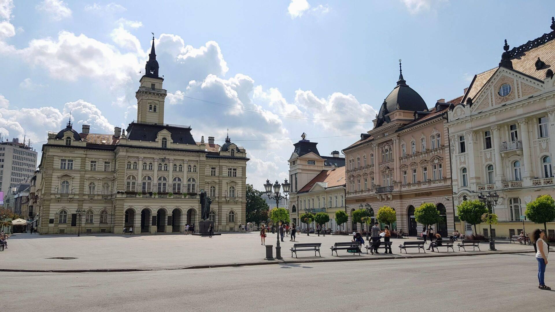 Ein weitläufiger historischer Stadtplatz, umgeben von Gebäuden mit österreichisch-ungarischer Architektur, Türmen und Kuppeln