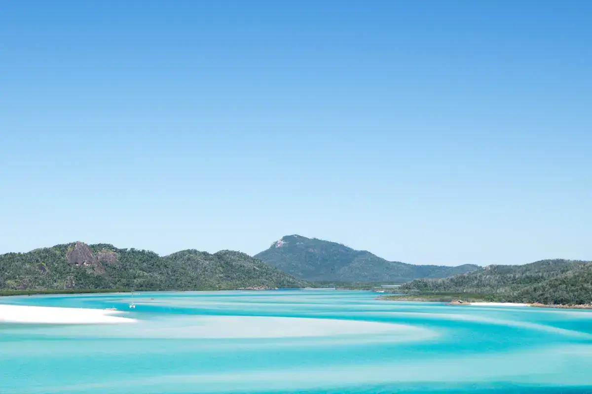 Laguna turquesa con playa de arena blanca, islas arboladas y montaña verde bajo un cielo azul despejado