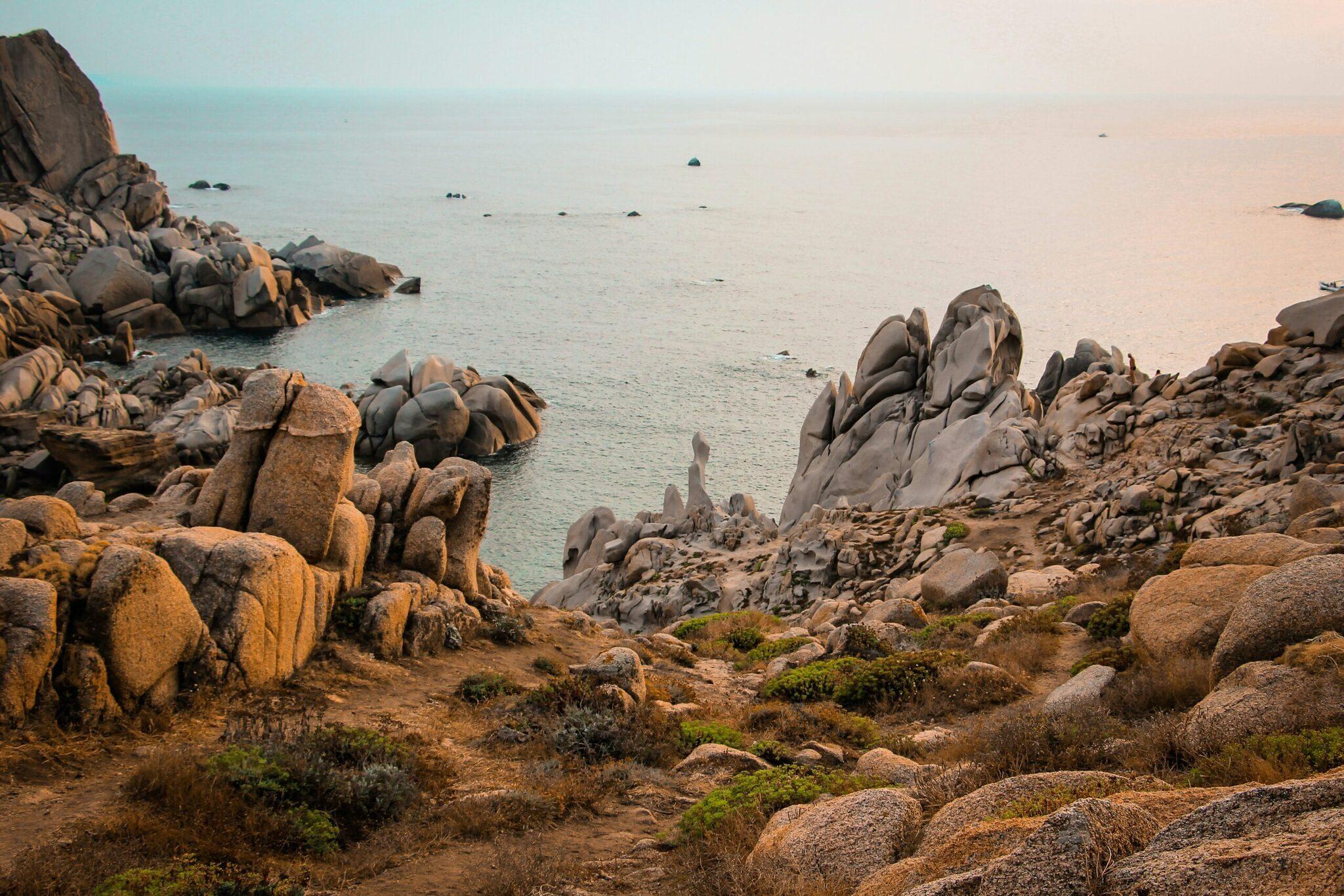 Costa rocosa granítica con formaciones de roca redondeadas que dominan una bahía tranquila de aguas turquesas