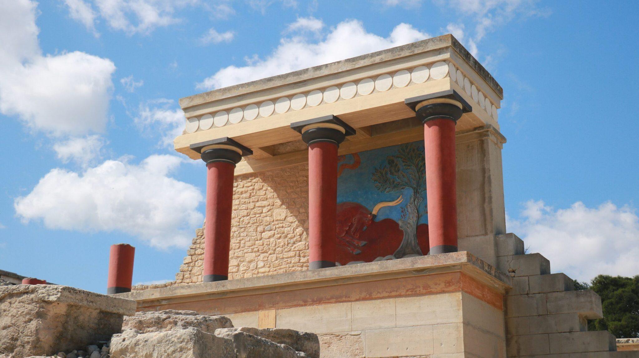 Ricostruzione di un antico palazzo minoico con colonne rosse e affreschi colorati sotto un cielo terso