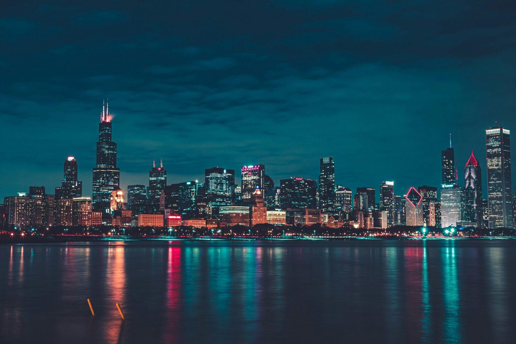 Beleuchtete Stadtskyline bei Nacht mit Wolkenkratzern, die sich im ruhigen Wasser eines Sees spiegeln