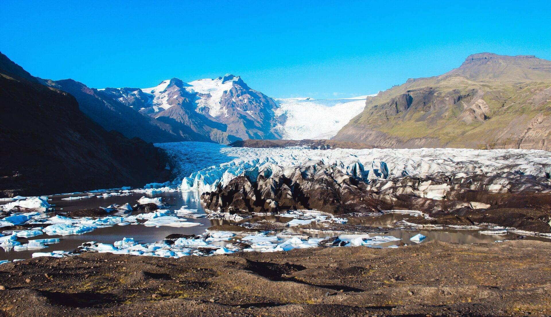 Un glaciar blanco y azul enmarcado por montañas rocosas con bloques de hielo flotando en un lago glaciar
