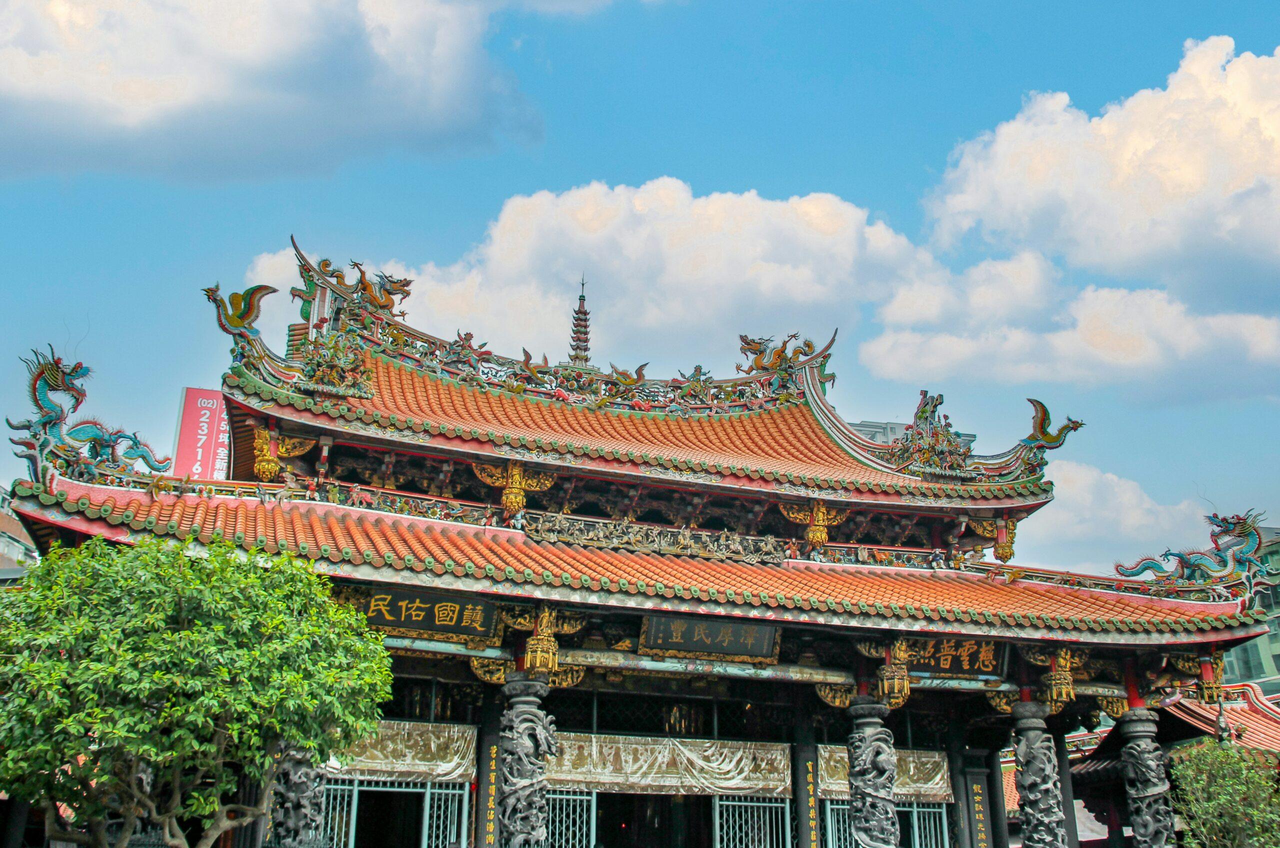 Templo budista asiático con tejados ornamentados en naranja y verde, dragones de colores y cielo despejado