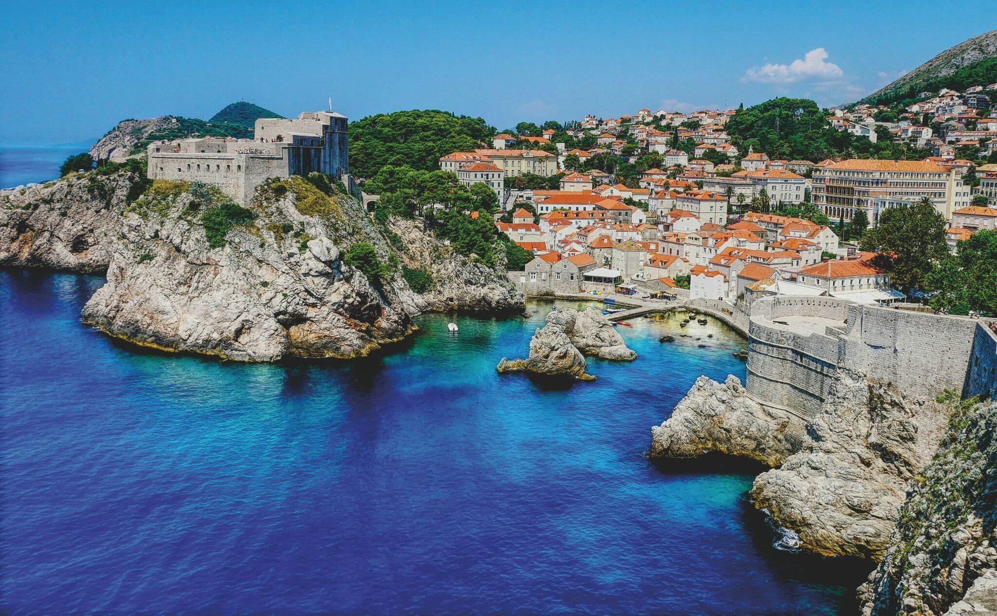 Vista panoramica di una città costiera medievale con fortificazioni su falesia rocciosa che domina una baia turchese