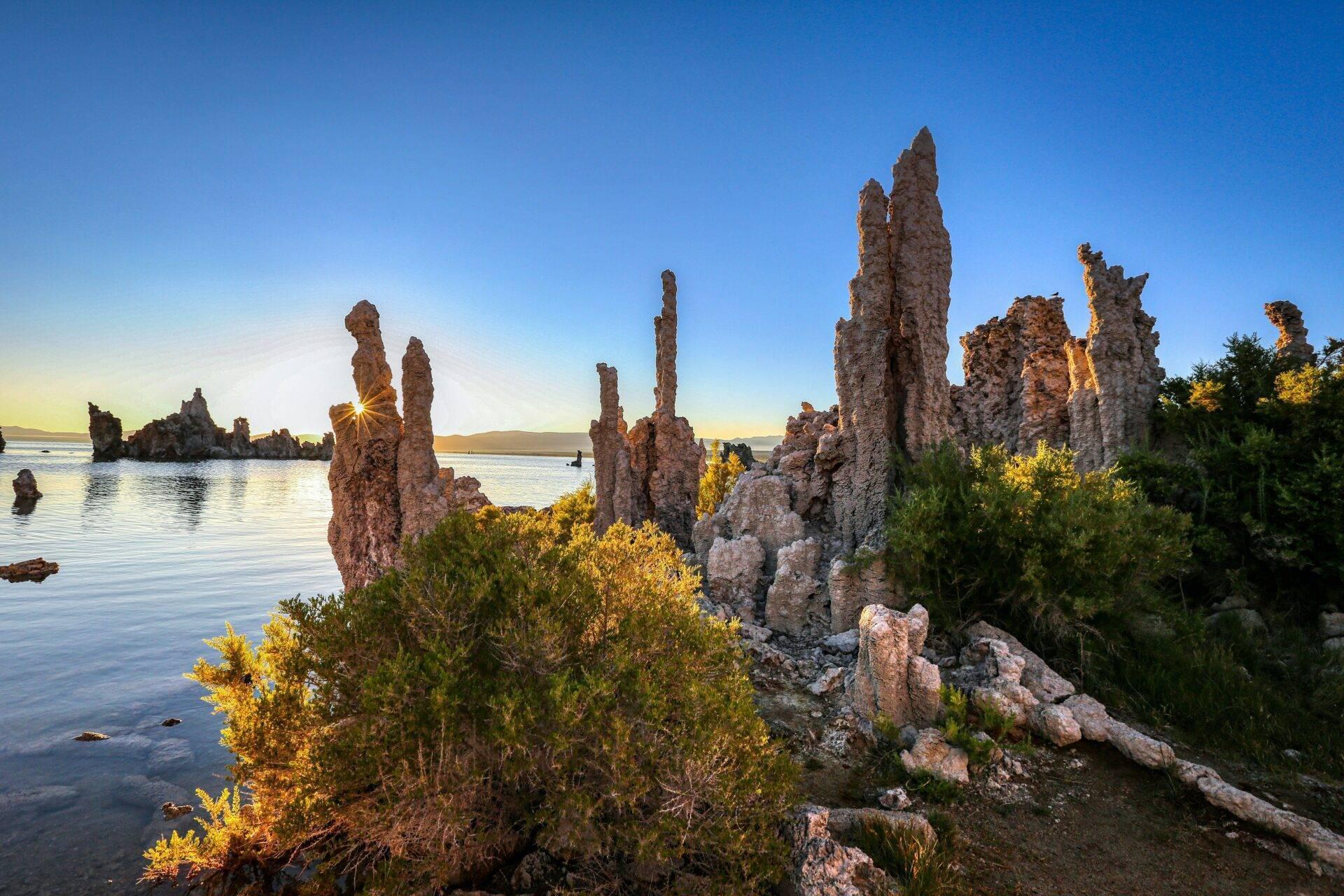 Formaciones rocosas en columnas que emergen de una bahía costera al atardecer, con vegetación verde