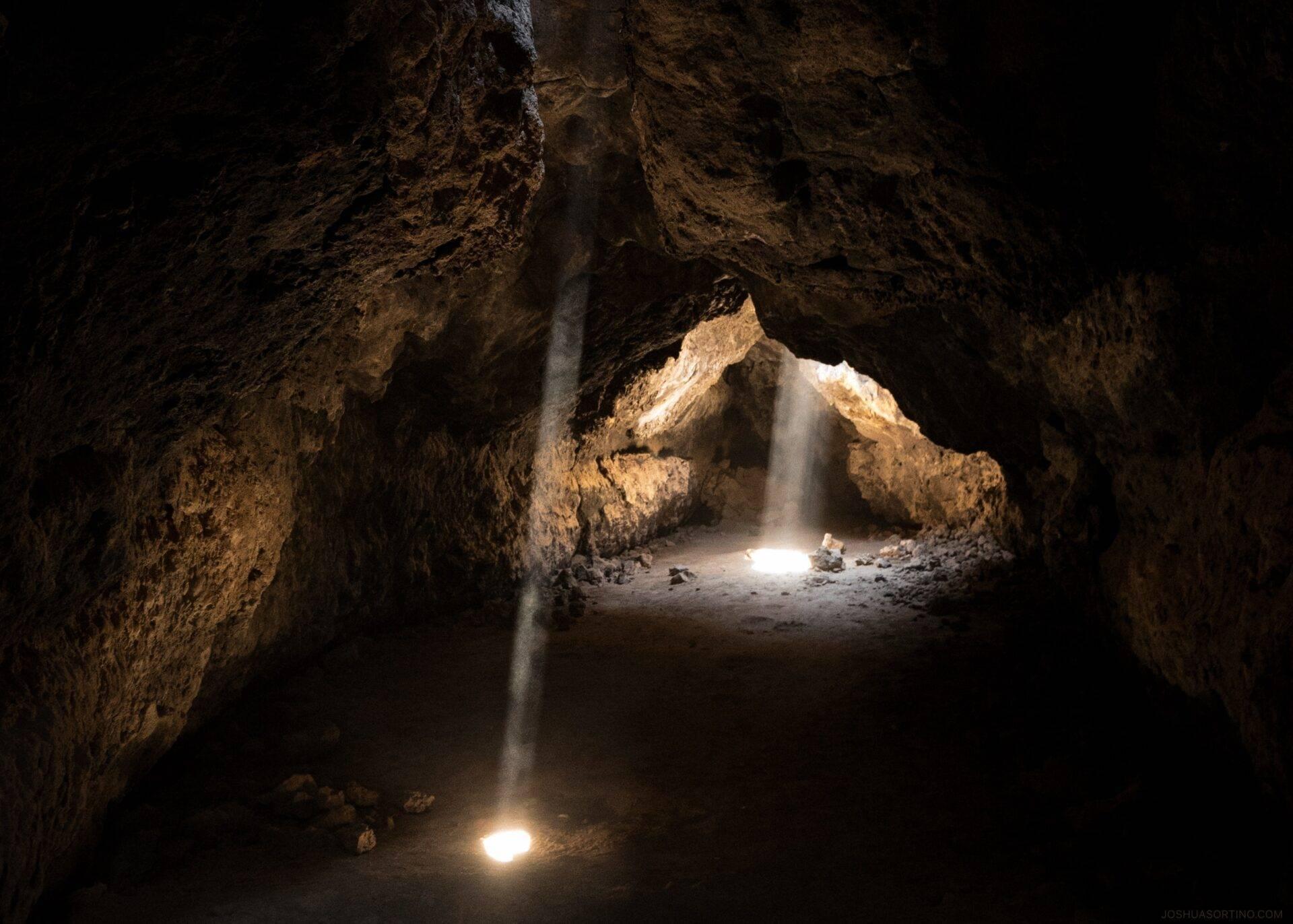 Interior de una cueva rocosa con rayos de luz atravesando la oscuridad e iluminando el suelo de roca