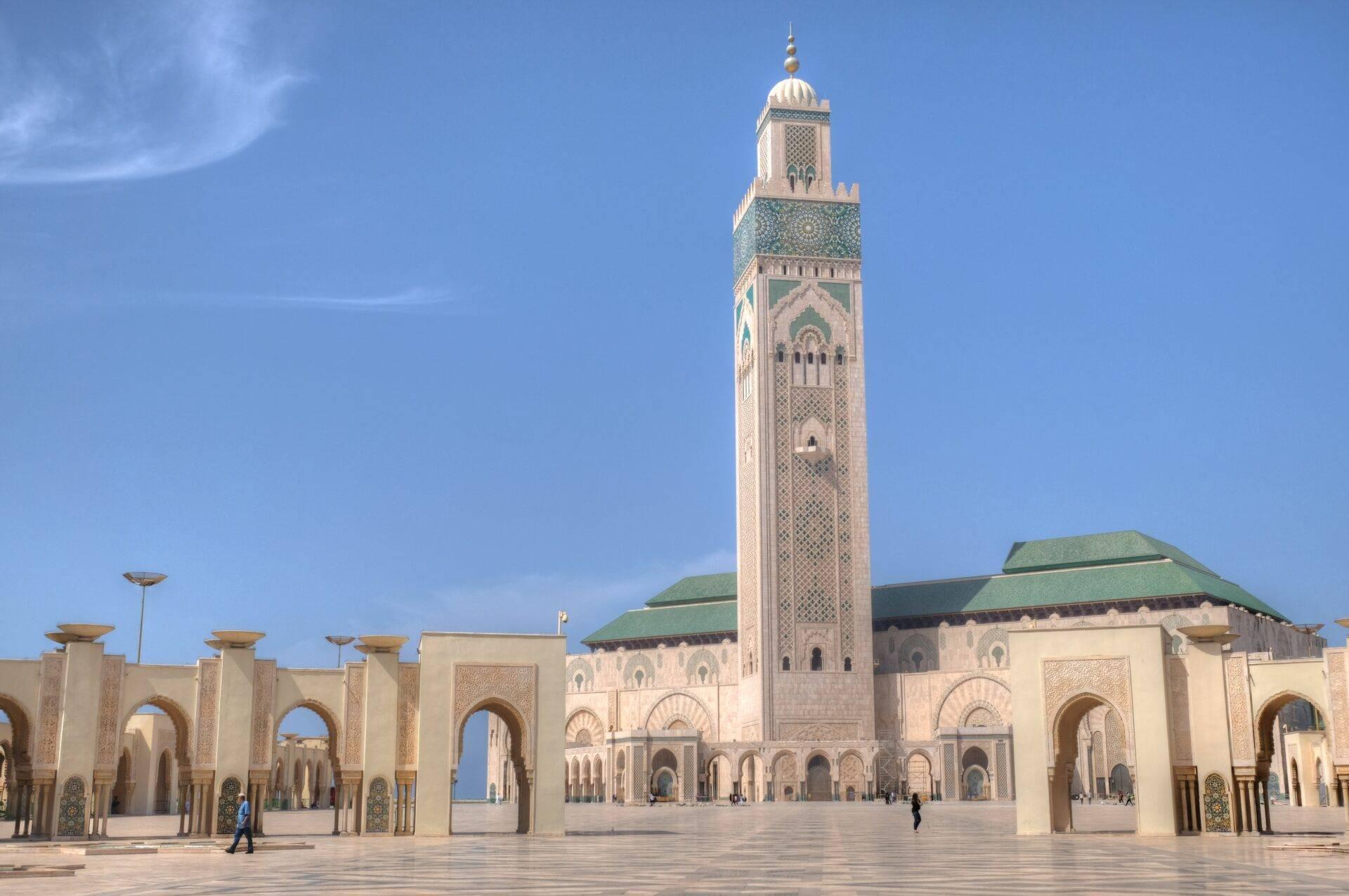Große Moschee mit schlankem weißen Minarett und gepflastertem Innenhof unter klarem blauen Himmel