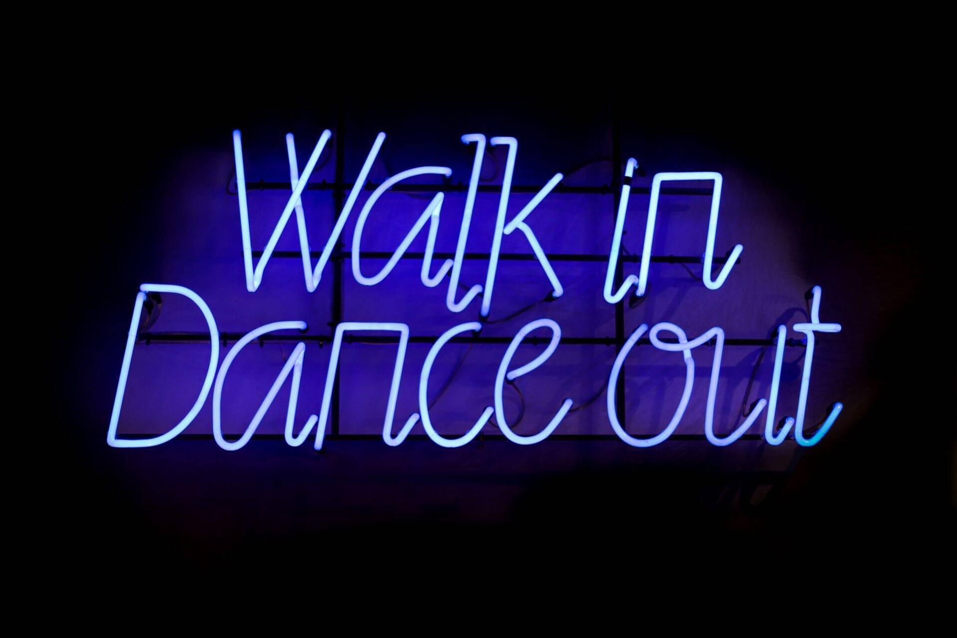 Leuchtende blaue Neonreklame mit dem Schriftzug „Walk in Danceout“ vor dunklem Hintergrund, urbane Nachtleben-Atmosphäre
