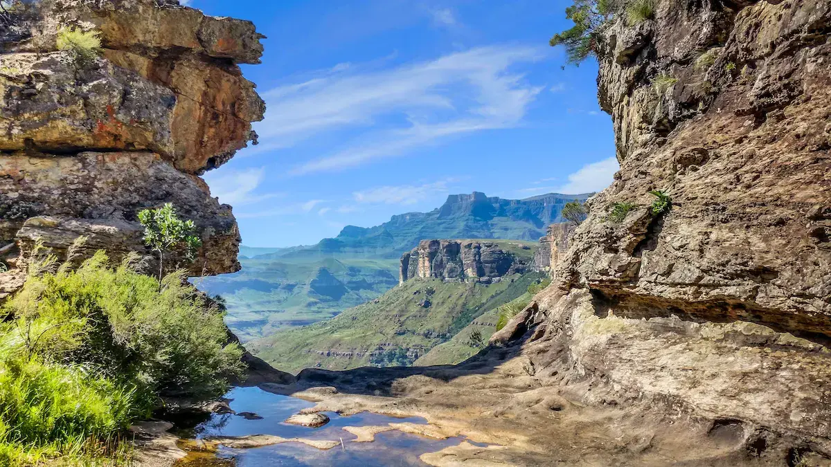 Vista desde una cueva rocosa sobre montañas escarpadas y verdes con un pequeño lago abajo